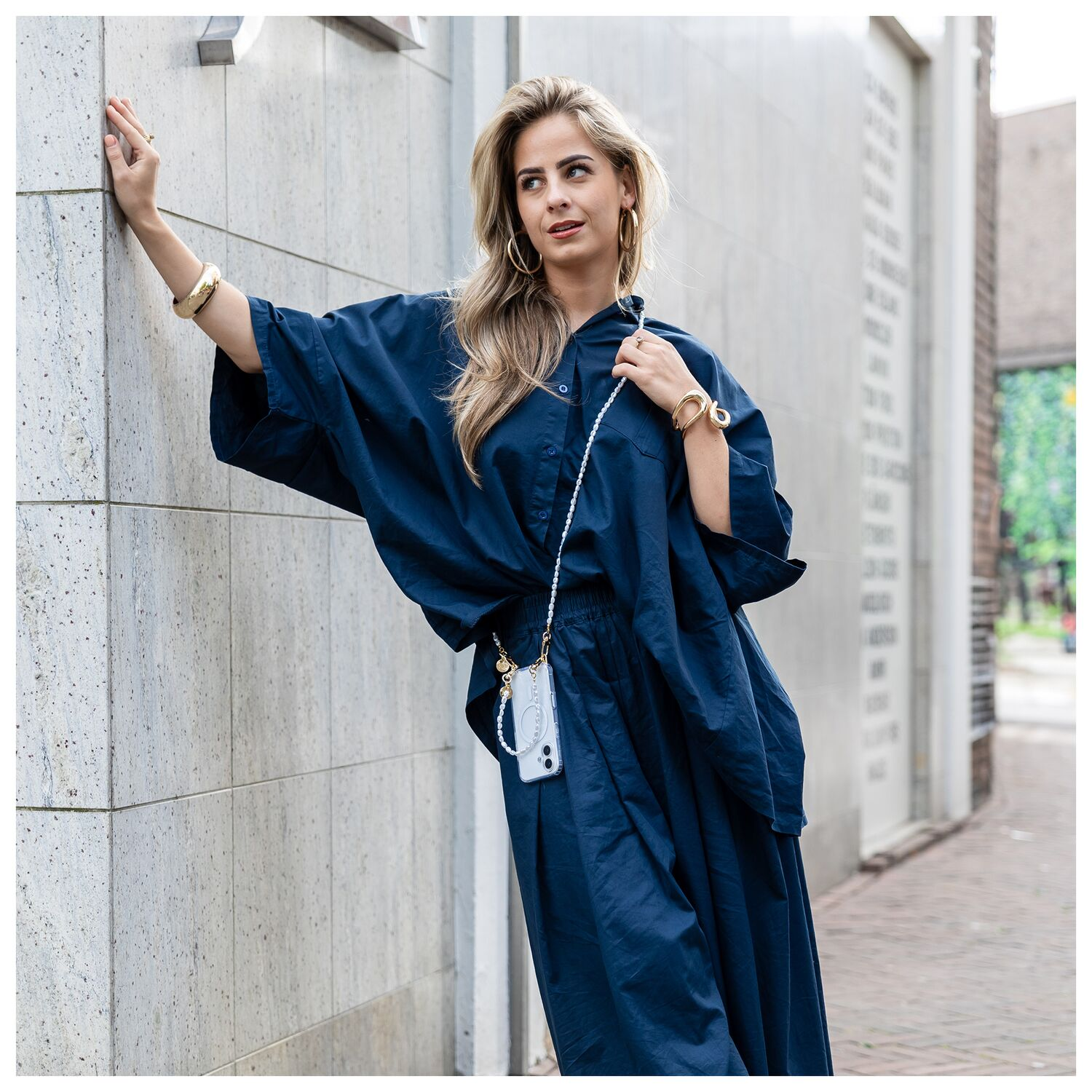 Een vrouw in een marineblauwe outfit leunt tegen een muur.
