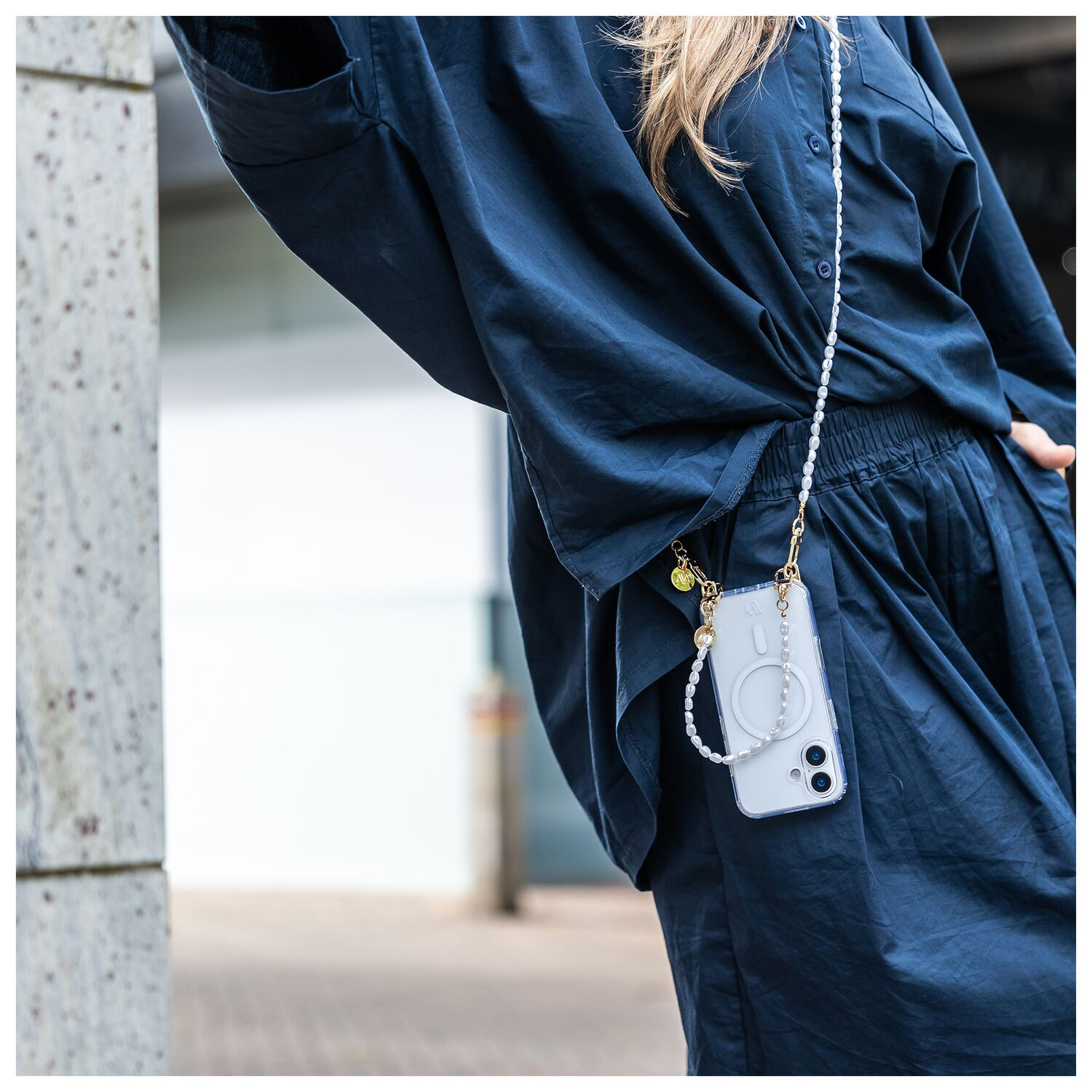 Een vrouw in een donkerblauw outfit draagt een telefoonhoesje versierd met parels.