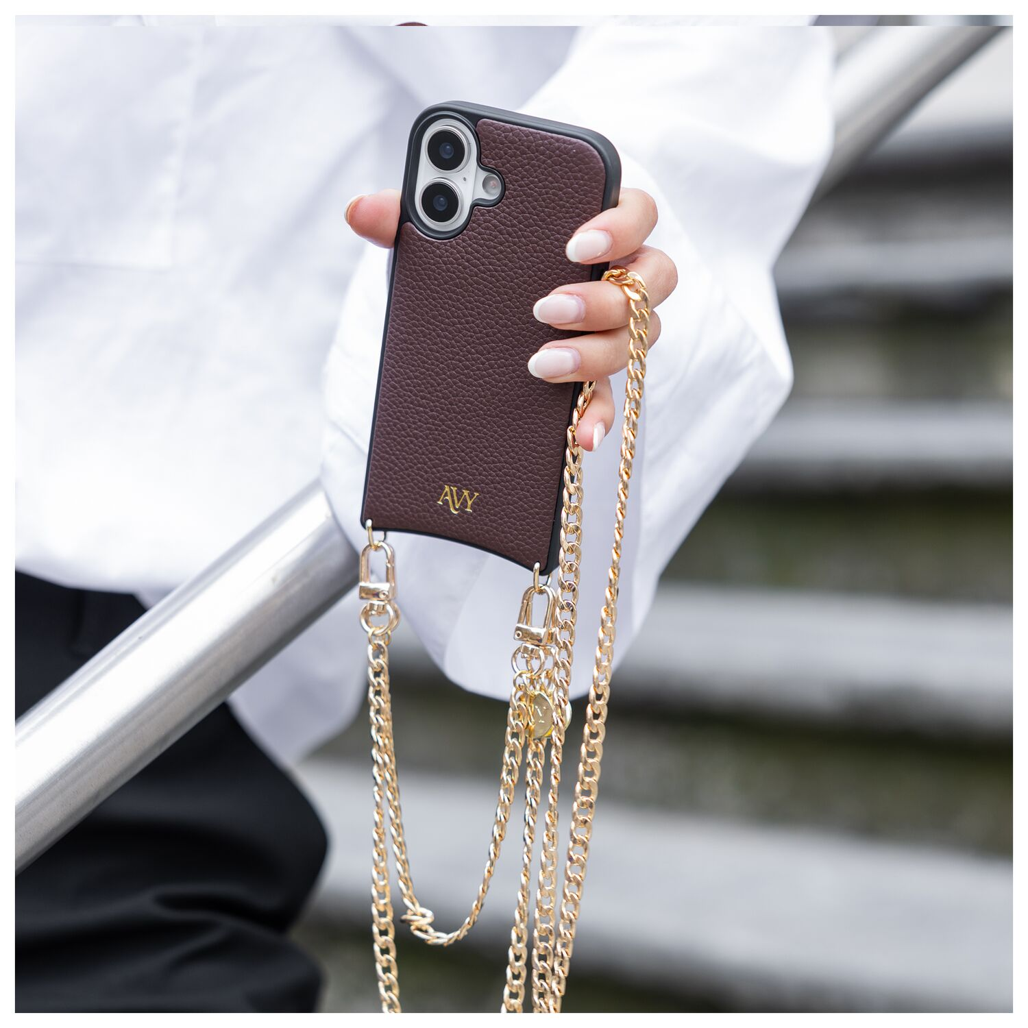 Bruine telefoonhoes met gouden ketting, vastgehouden door een gemanicuurde hand.