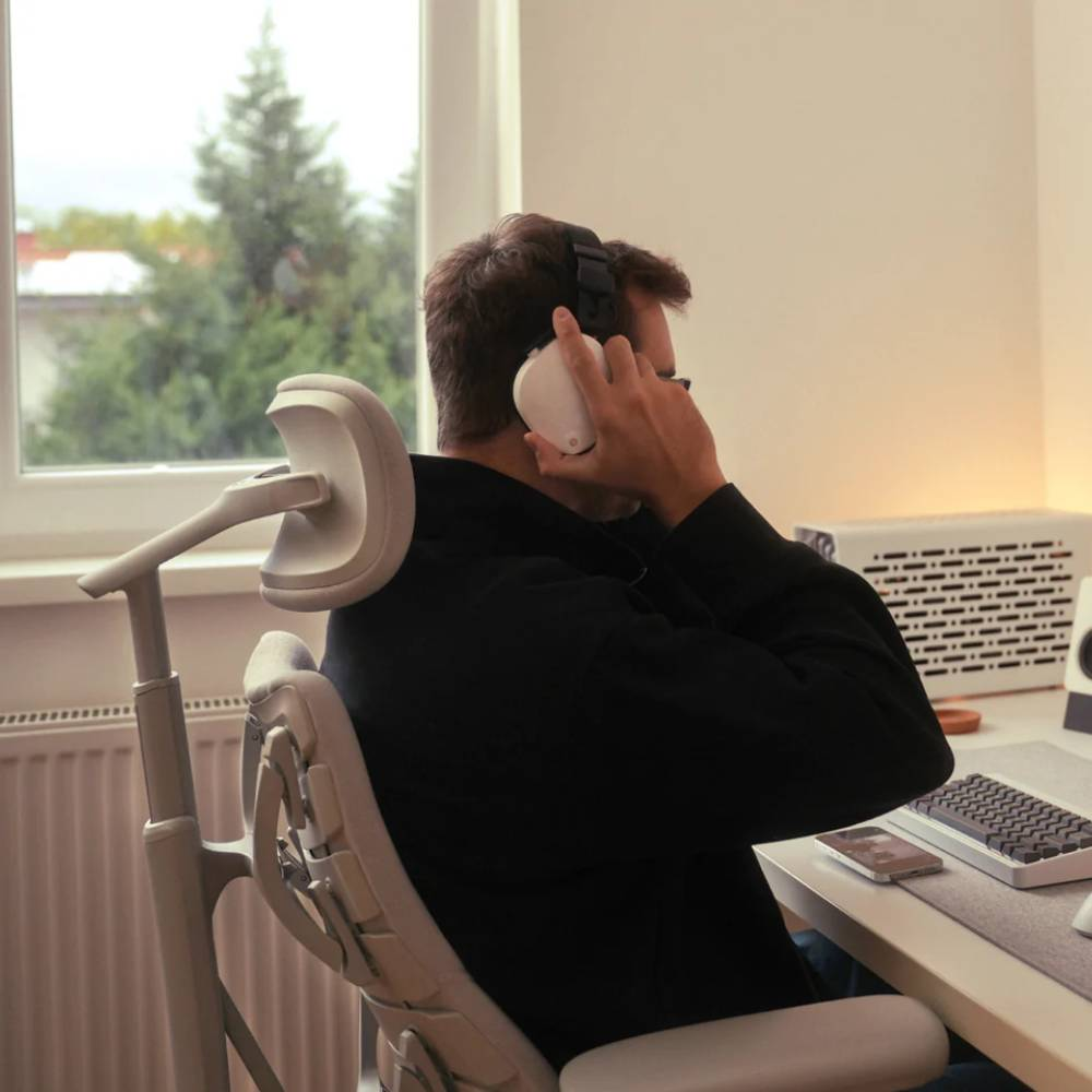 Mann mit Kopfhörern sitzt am Schreibtisch, blickt aus dem Fenster.