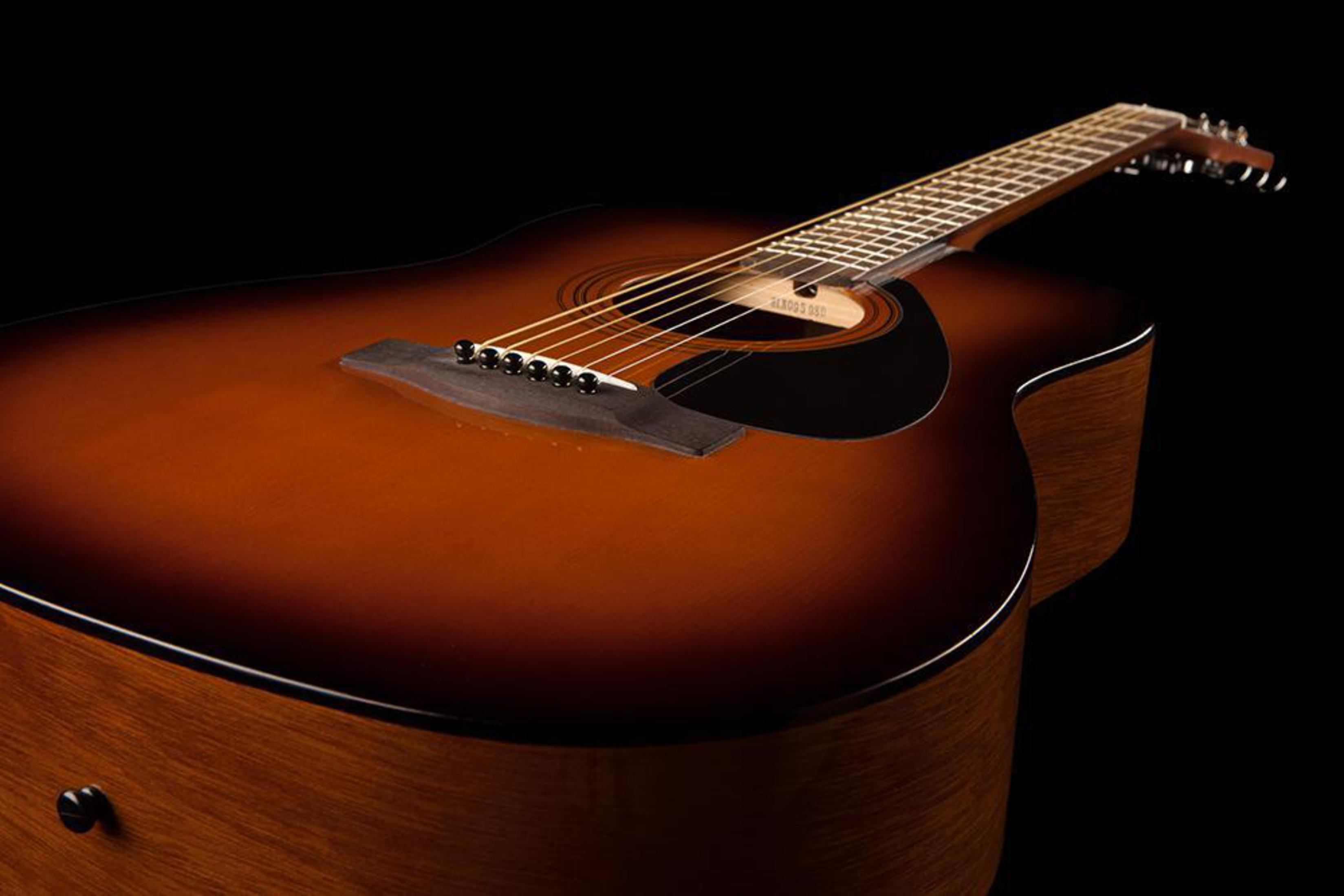 Eine Akustikgitarre mit braunem Korpus und schwarzen Details auf schwarzem Hintergrund.