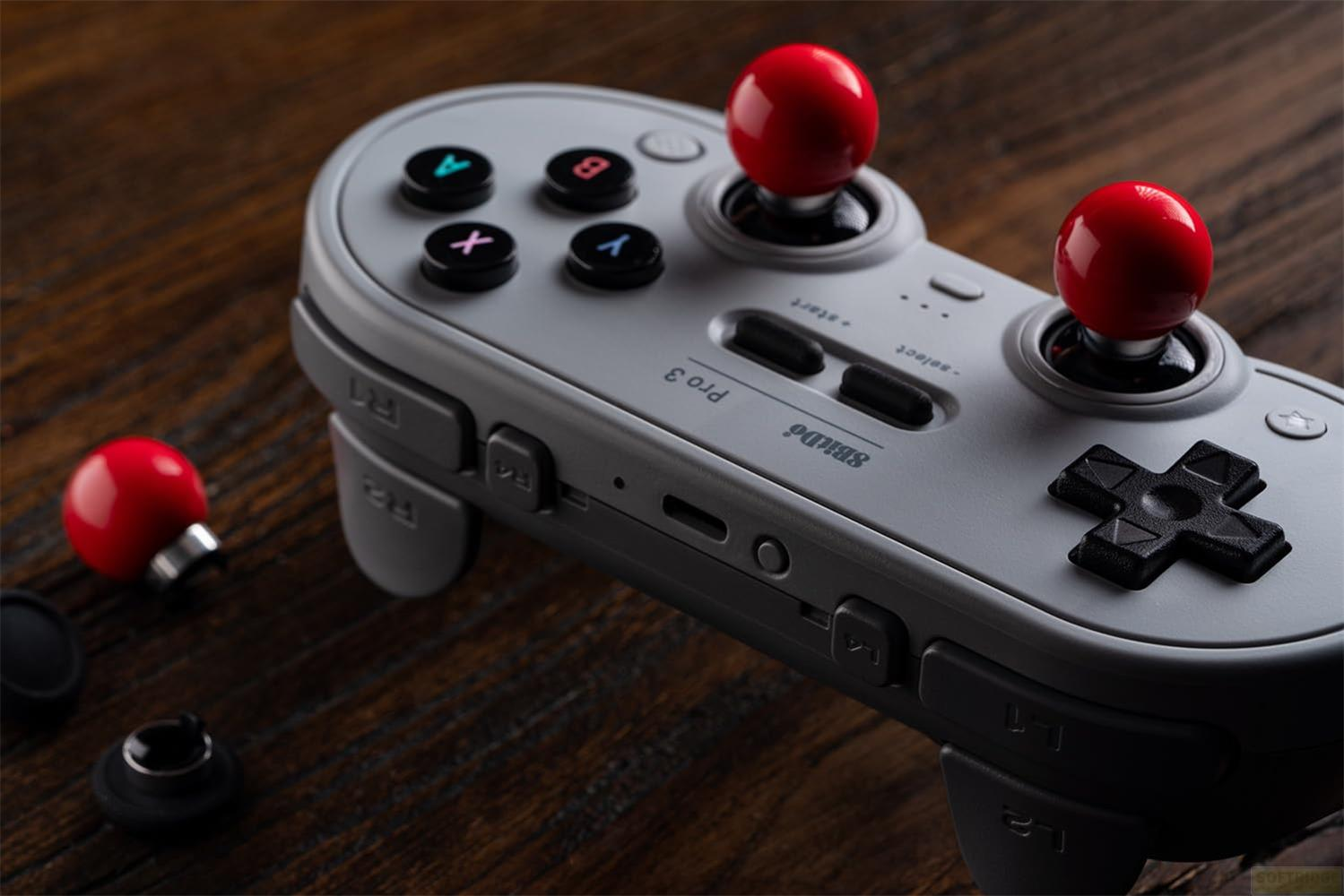 Szary kontroler do gier z czerwonymi kulkami joysticka na drewnie.