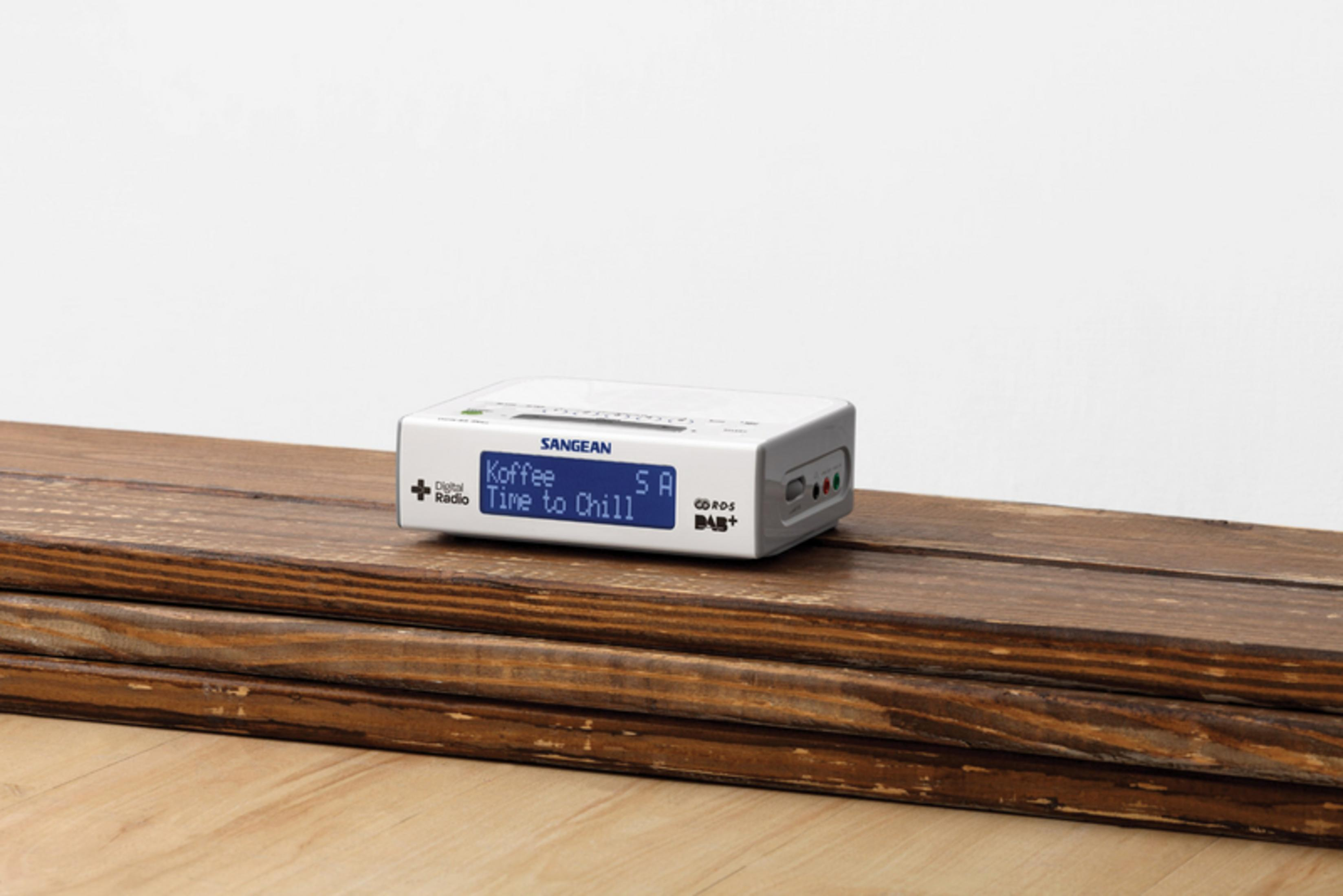 Una radio digitale Sangean bianca con schermo blu poggia su assi di legno.