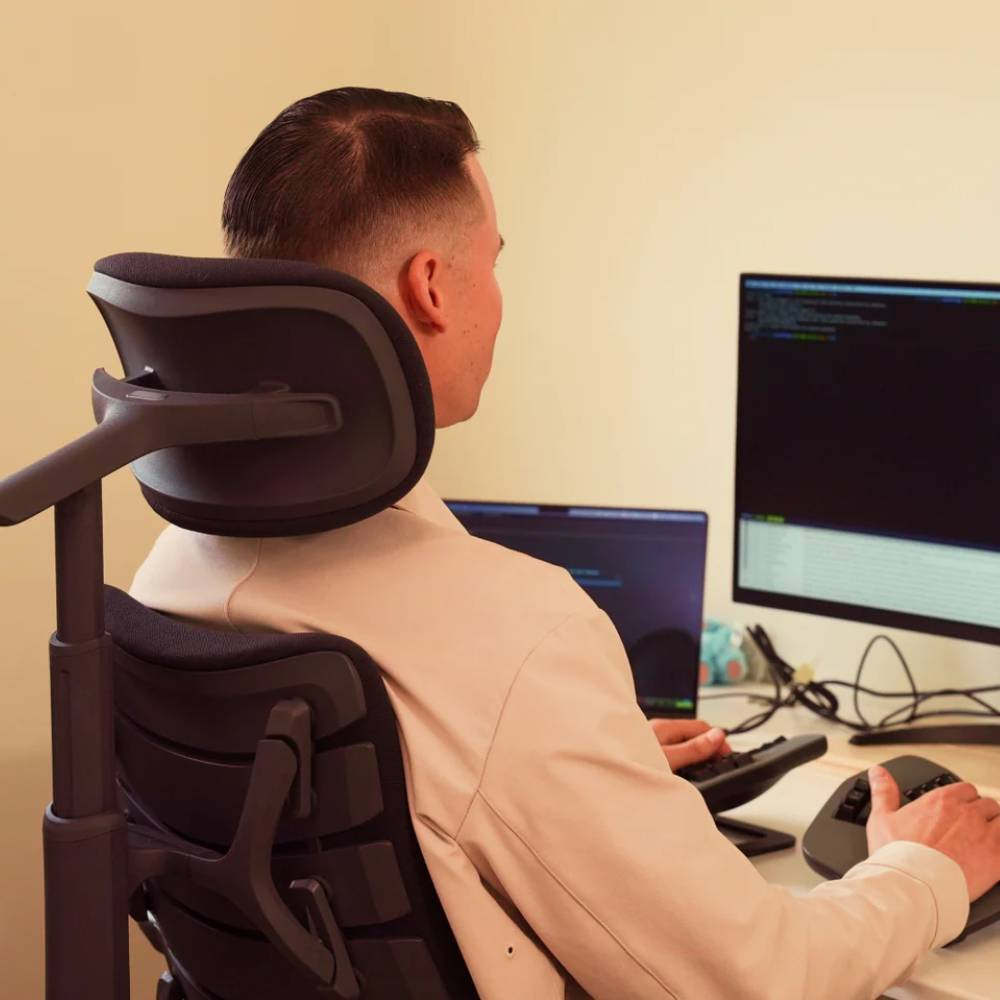 Mann in beige Hemd am Schreibtisch, blickt auf Computermonitore, benutzt Tastatur und Maus.