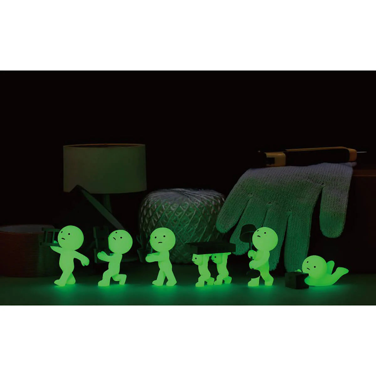 Leuchtende Figuren stehen auf einem Tisch mit einem Handschuh, Garn und einer Lampe.