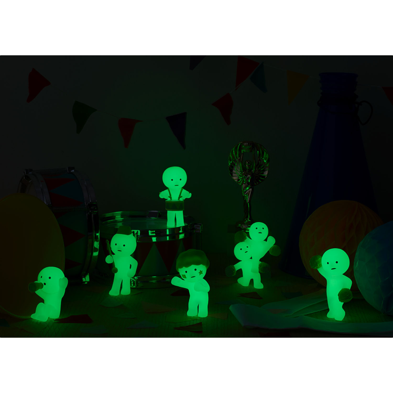 Leuchtende Figuren auf einer Party-Szene mit Trommel, Pokal und Girlanden.