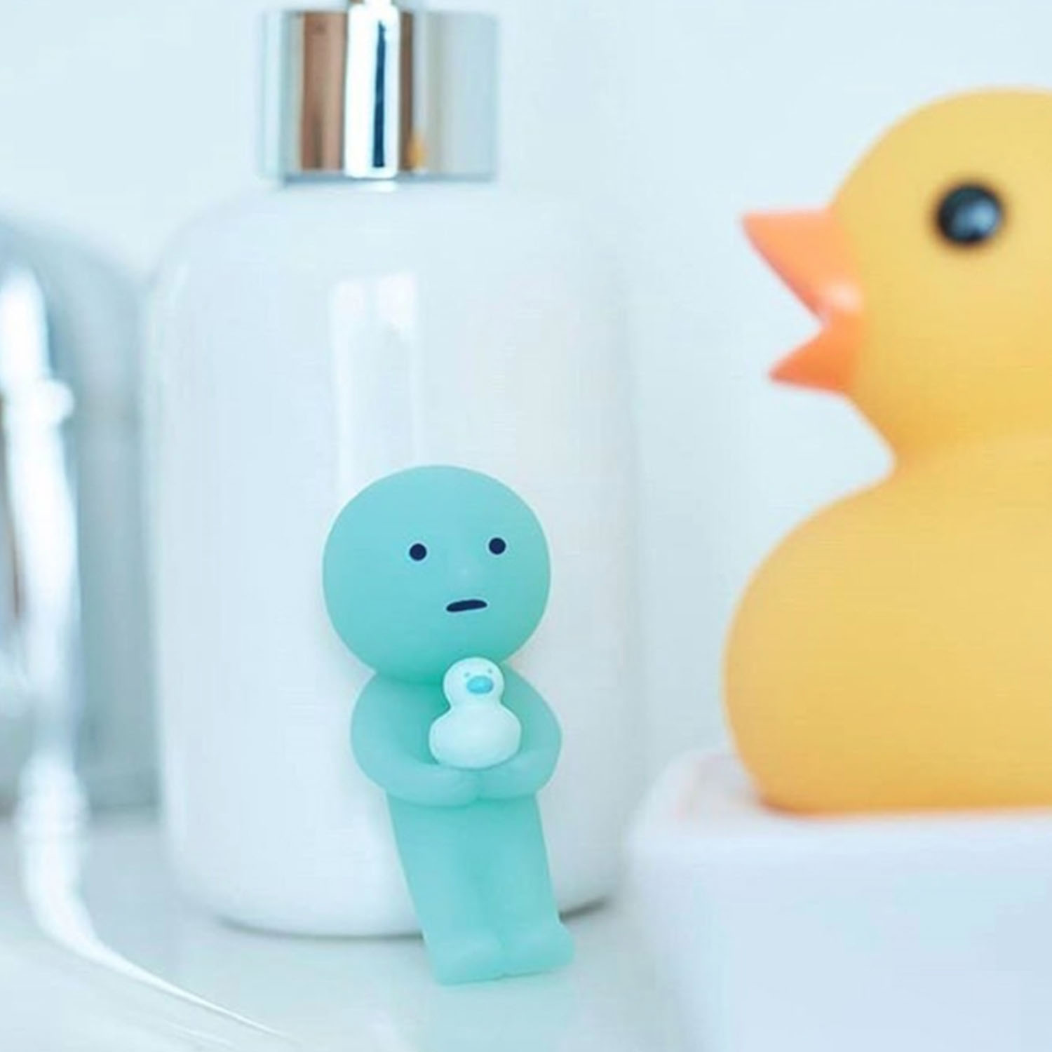 Eine blaue Figur hält eine kleine weiße Ente. Eine gelbe Ente ist im Hintergrund.