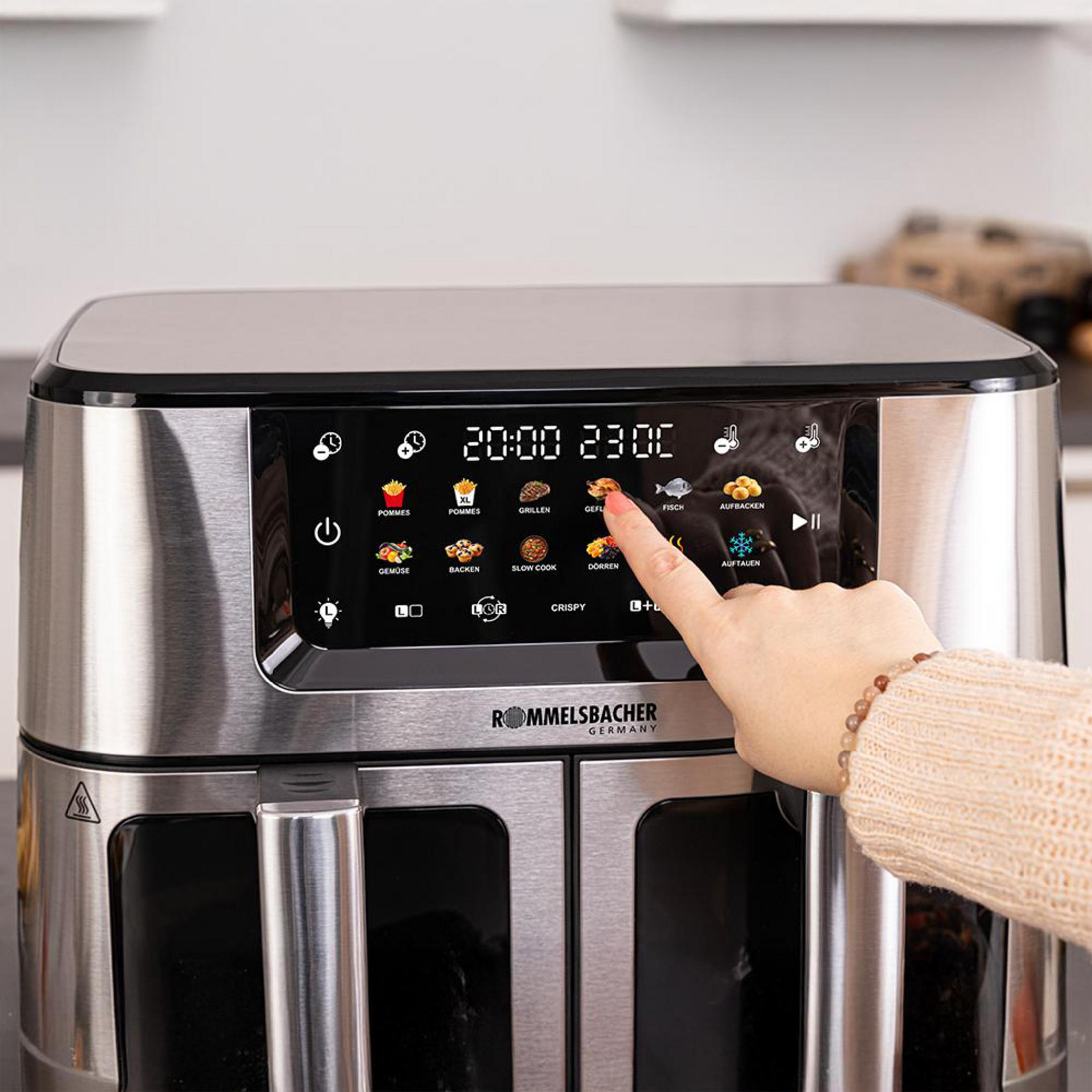 Eine Hand tippt auf ein Bedienfeld mit Kochsymbolen und Timer auf einem silbernen Airfryer.