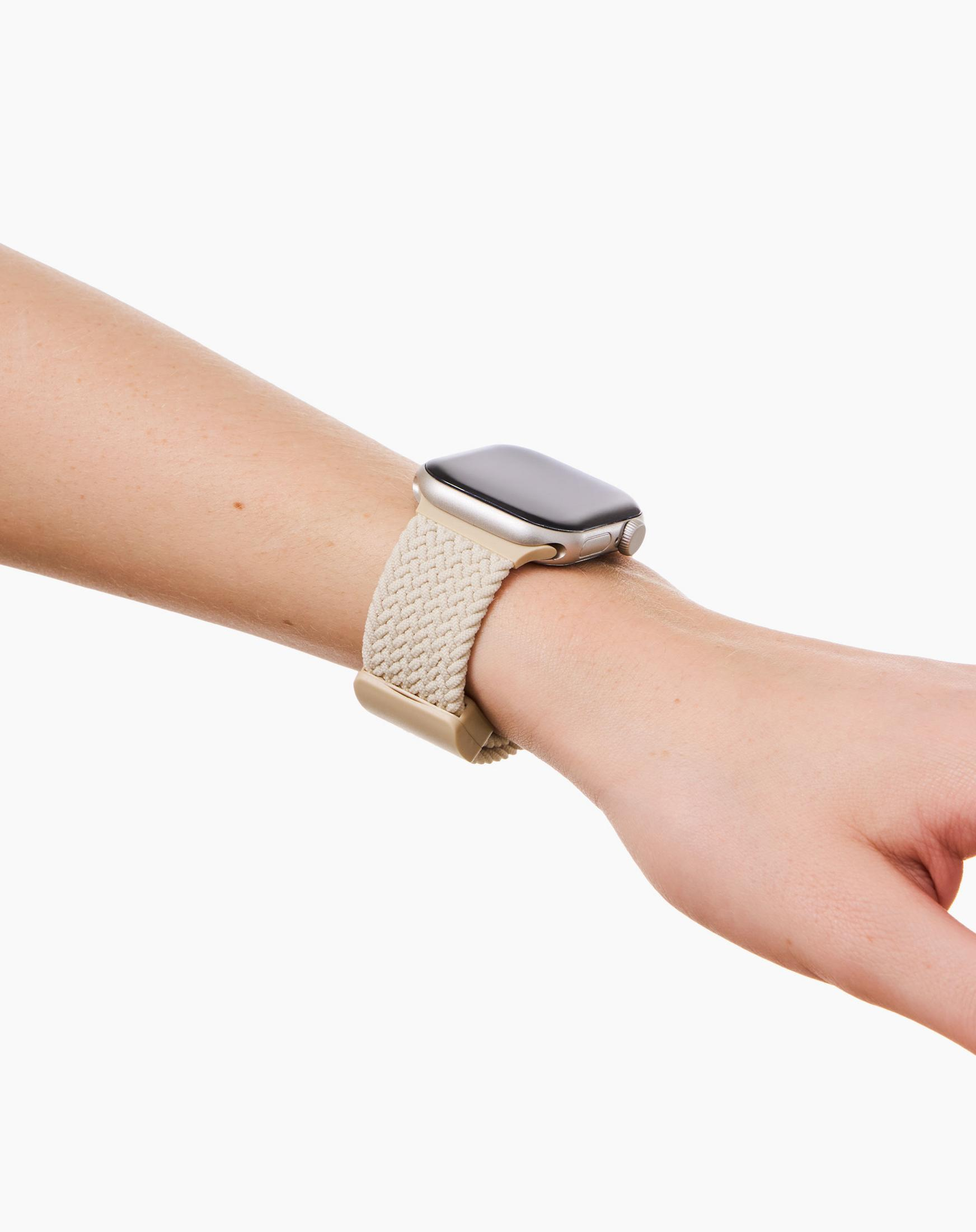 Eine Hand trägt eine silberne Smartwatch mit einem hellbeigen geflochtenen Armband.