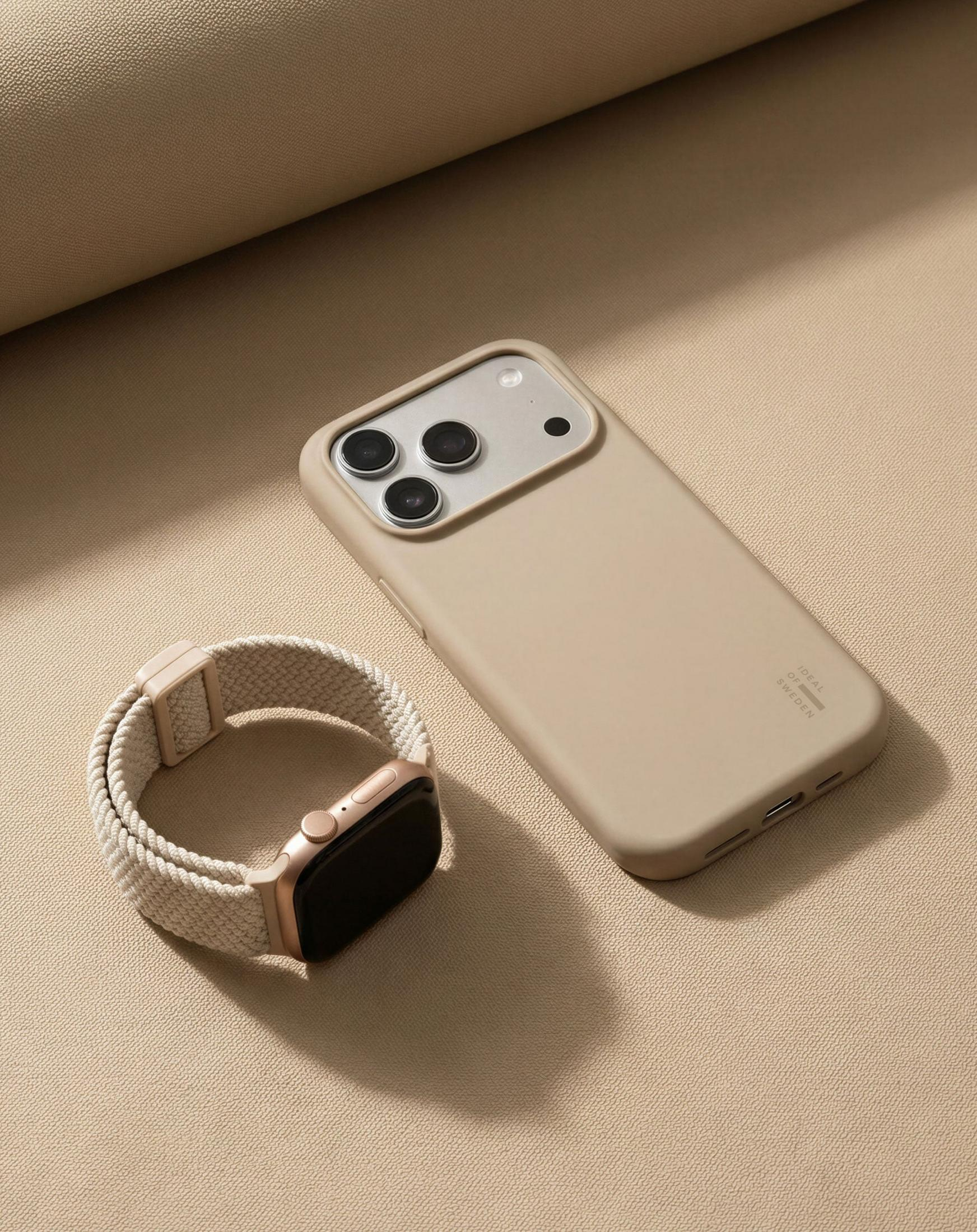 Ein beige Handyhülle und eine goldene Smartwatch liegen auf beigem Stoff.