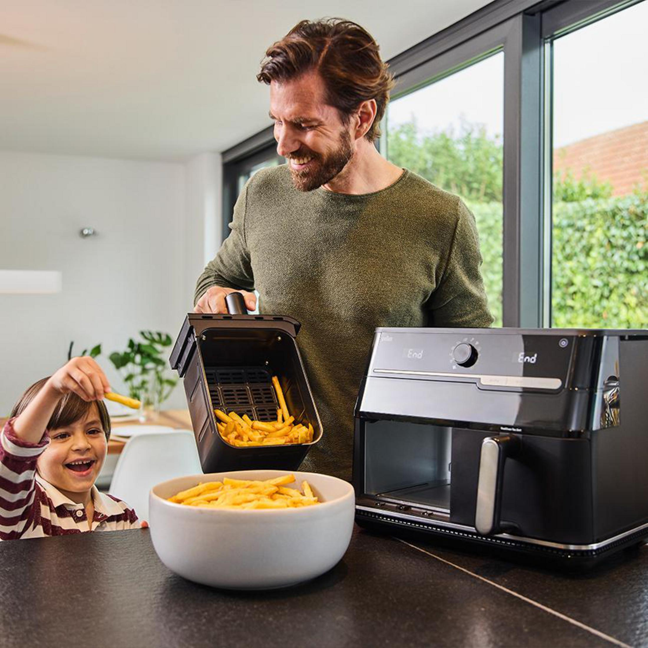 Un uomo e un bambino con patatine fritte accanto a una friggitrice ad aria nera.