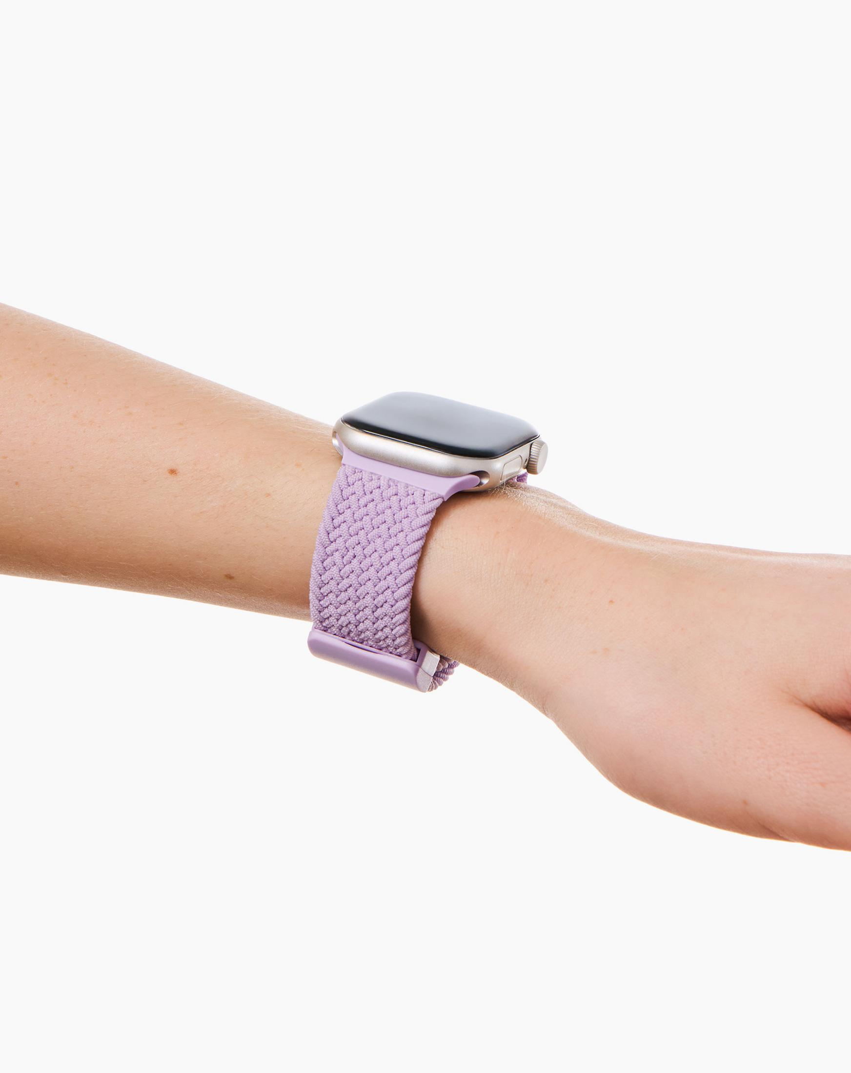 Ein Arm trägt eine silberne Smartwatch mit einem lavendelfarbenen gewebten Armband.