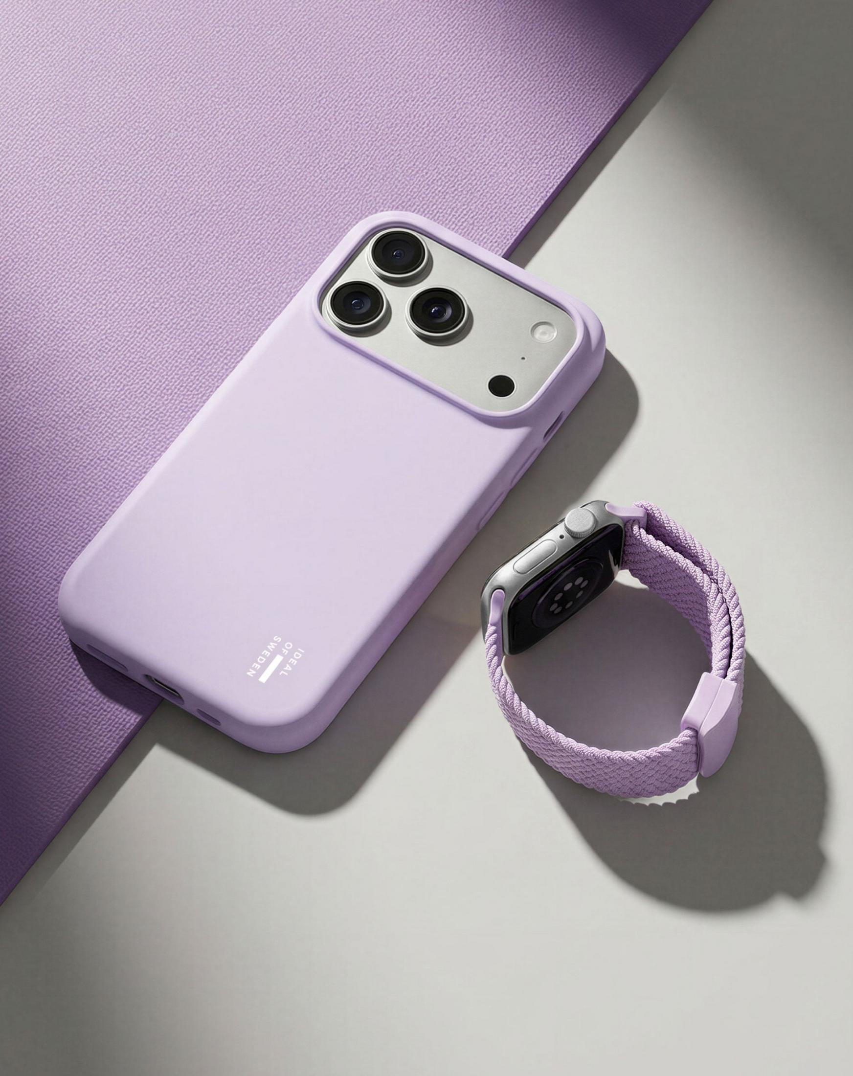 Ein lila iPhone-Case und eine Apple Watch mit lila Band liegen nebeneinander auf einem grauen Untergrund.