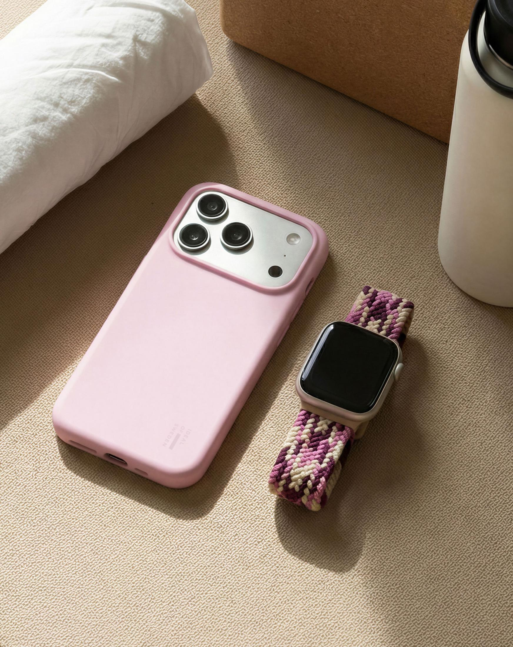 Ein rosafarbenes Handy mit drei Kameras neben einer Smartwatch mit geflochtenem Band.