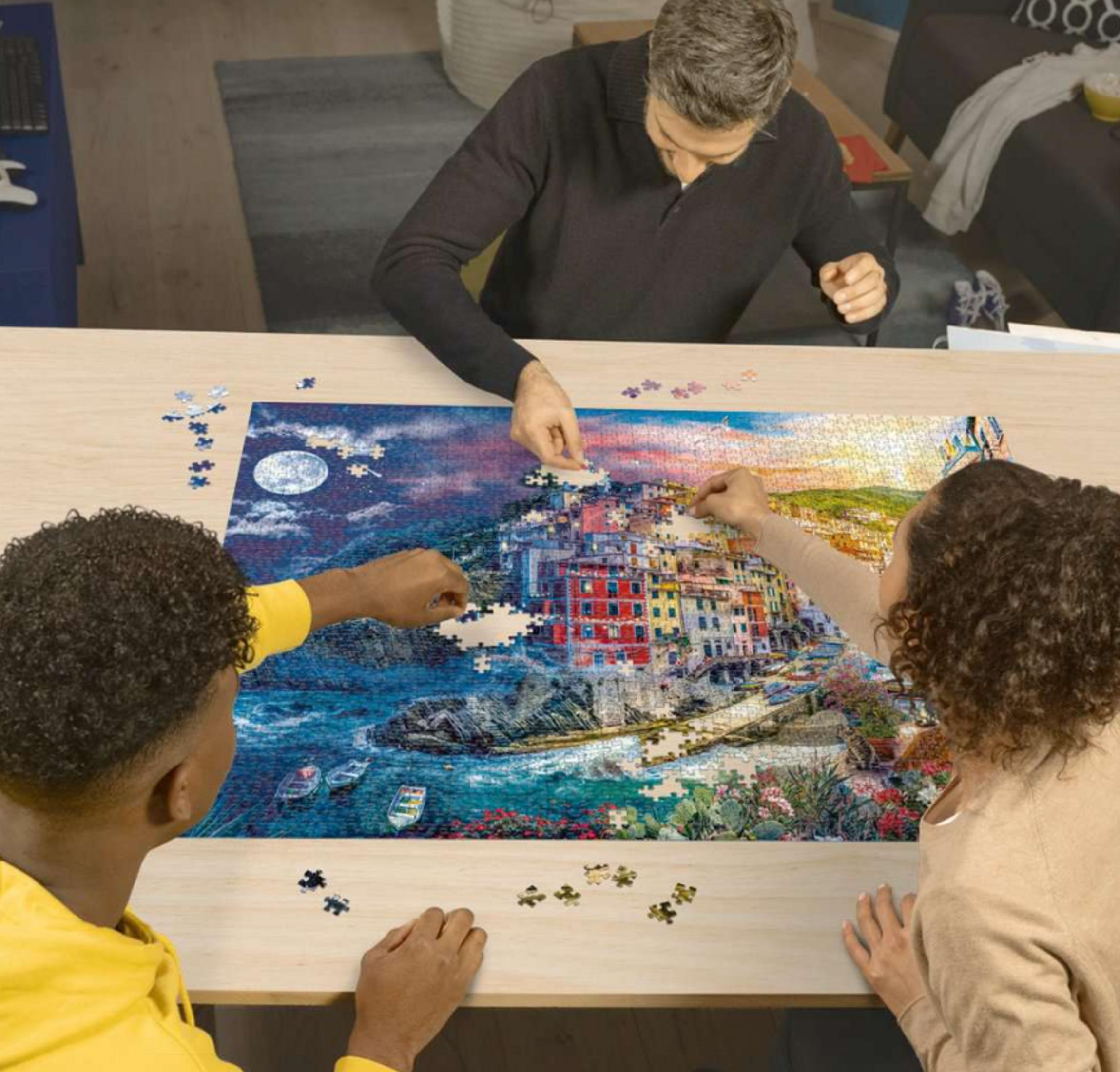 Drei Personen bauen ein Puzzle eines Küstenortes bei Tag und Nacht.