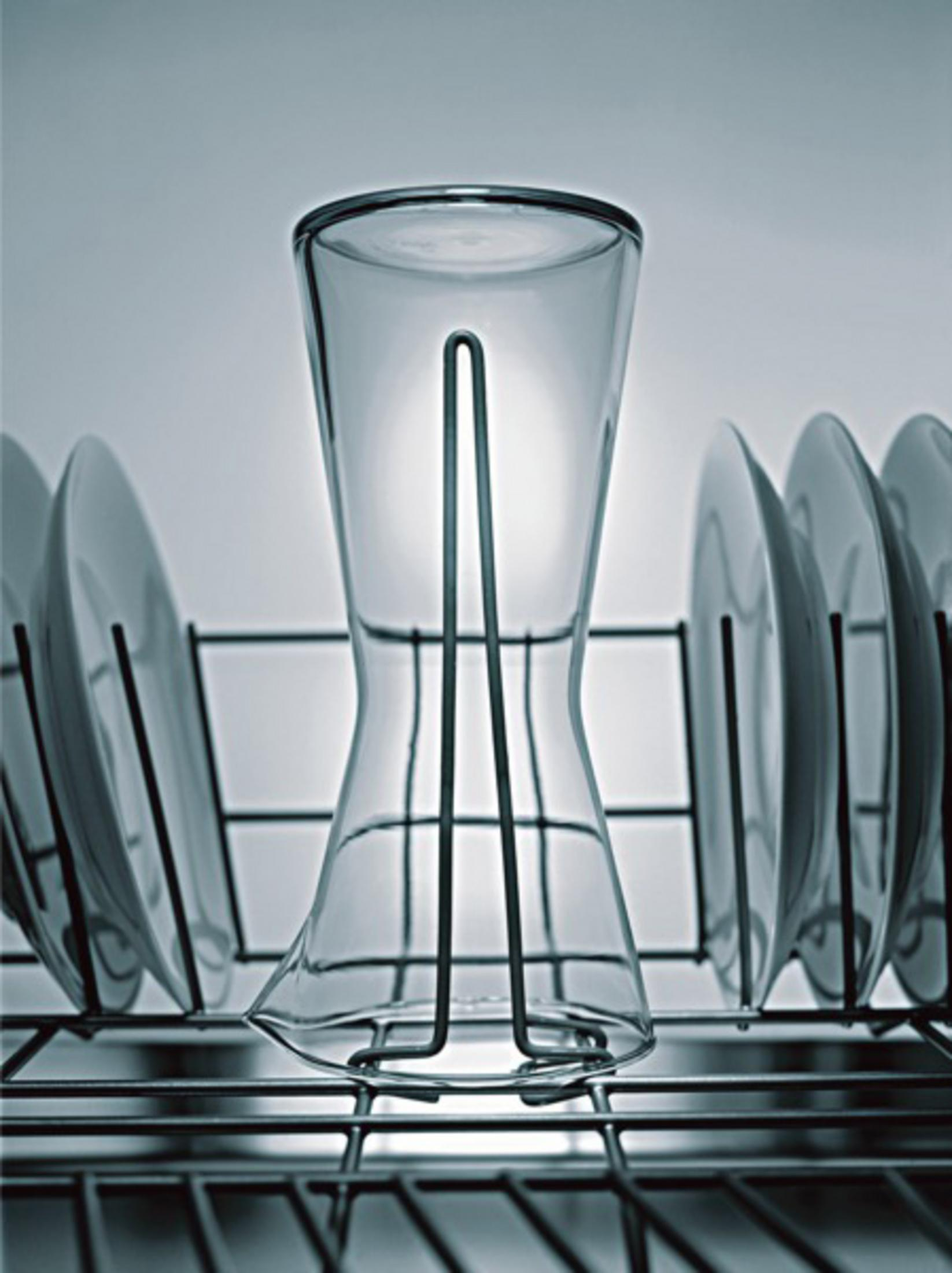 Ein Glas steht aufrecht in einem Abtropfgestell neben mehreren Tellern.