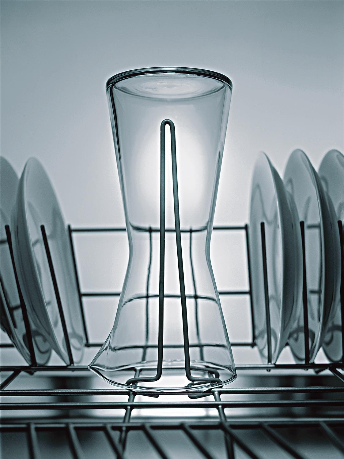 Ein Glas steht in einem Abtropfgestell zwischen Tellern.