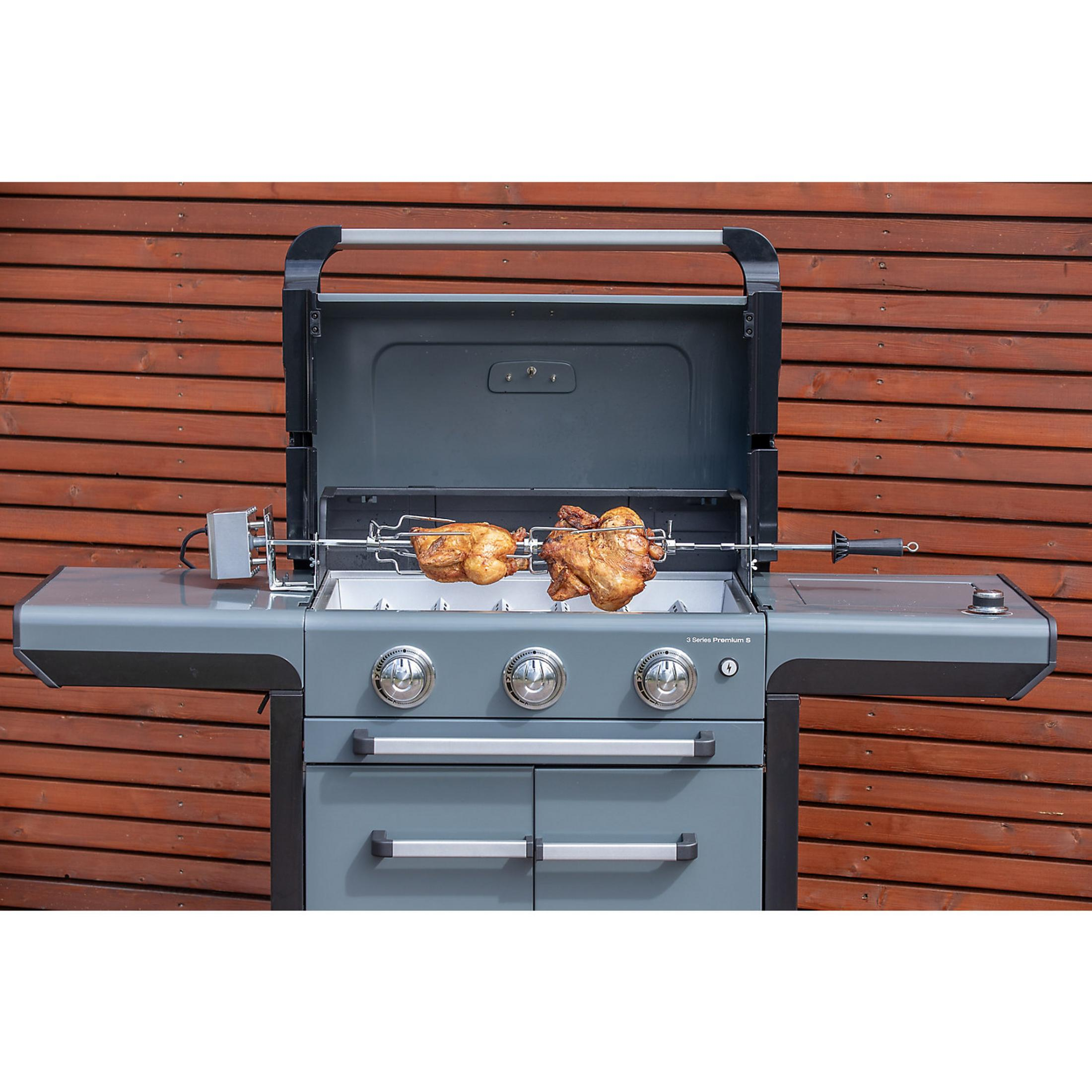 Zwei Hähnchen werden auf einem Drehspieß über einem Gasgrill gegrillt.
