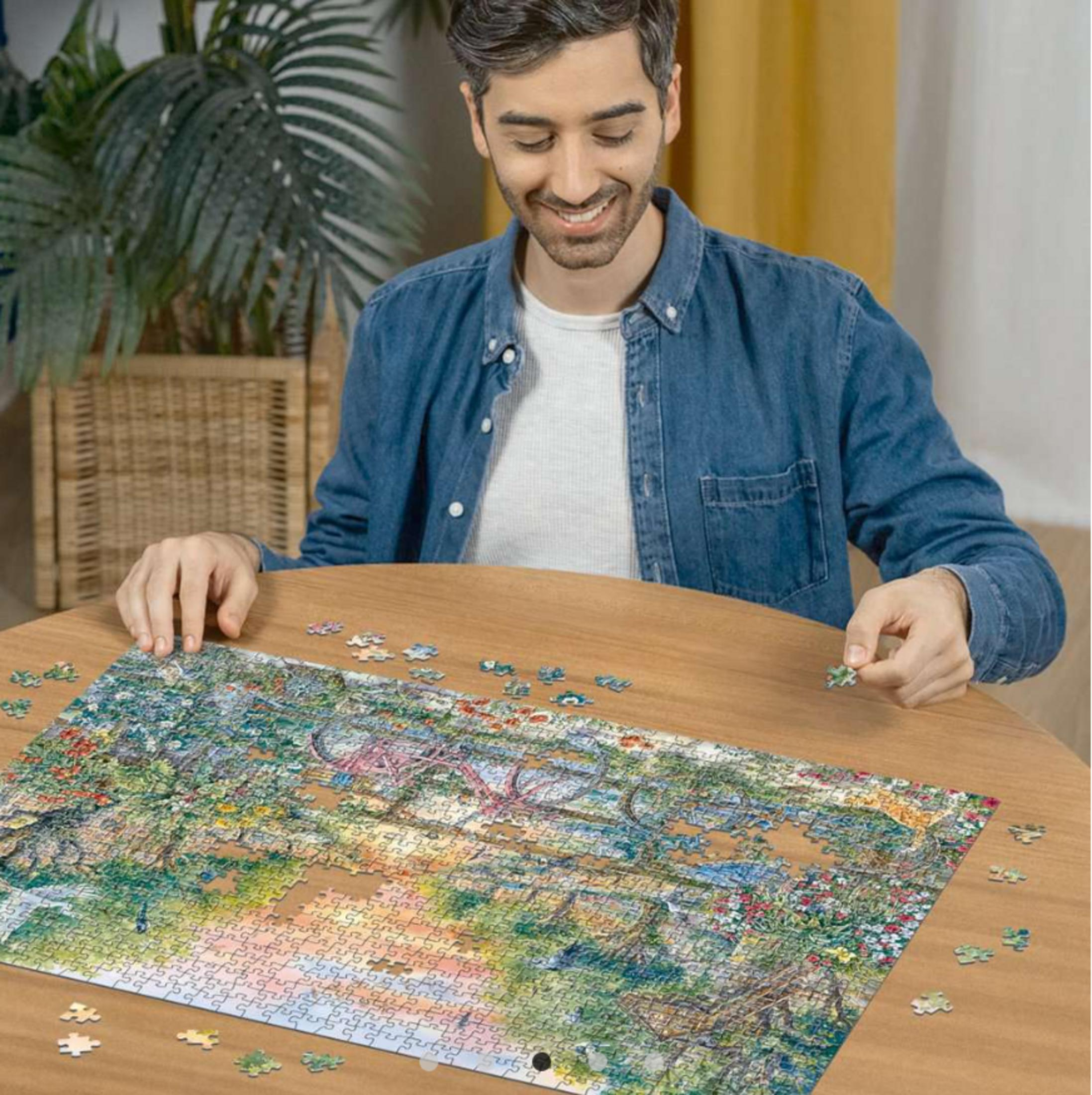 Mann sitzt an einem Holztisch und legt ein Puzzle mit vielen bunten Teilen zusammen.