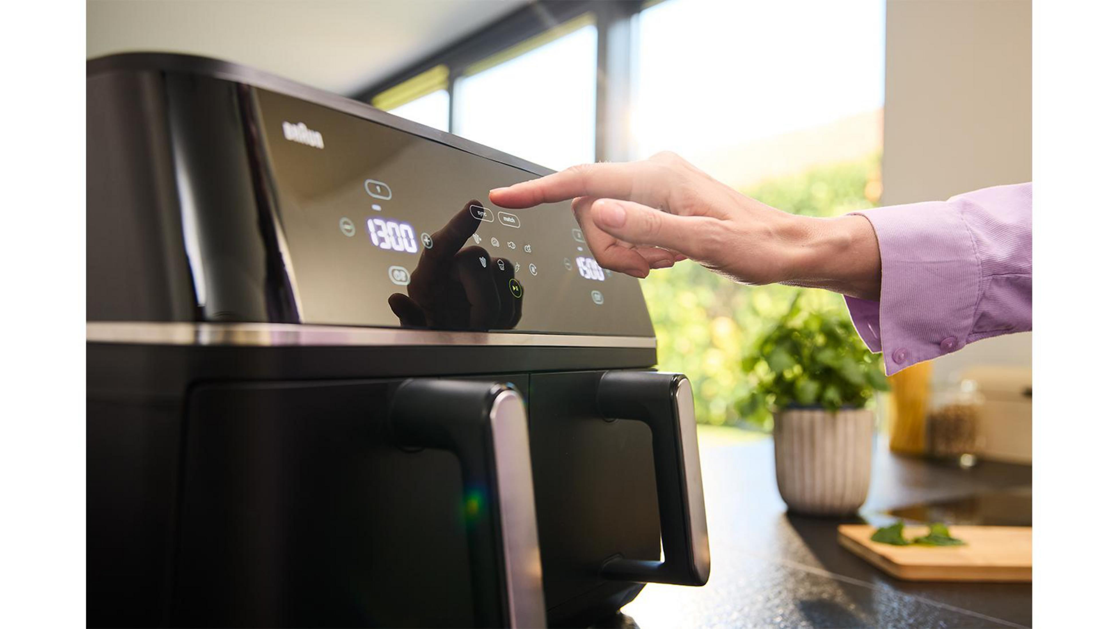 Eine Hand drückt auf das Touchpad eines schwarzen Heißluftfritteusen-Bedienfelds.