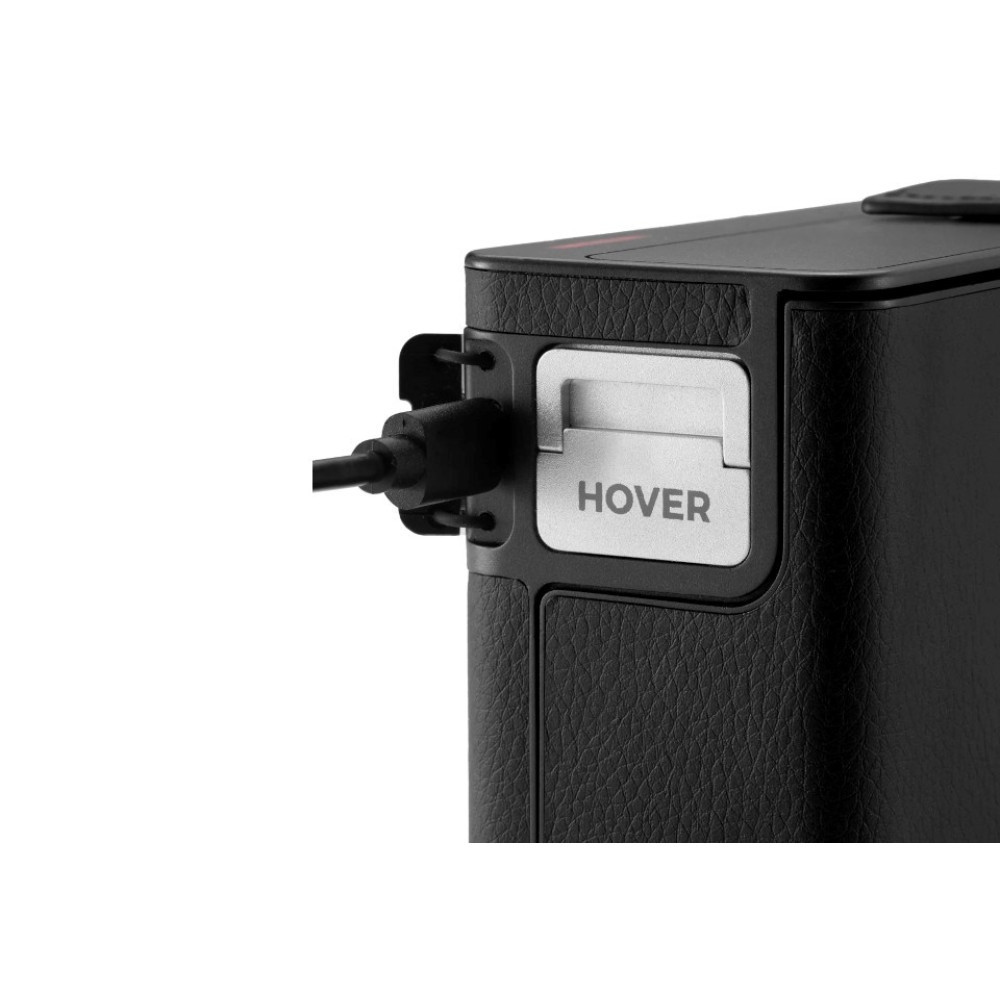 Ein schwarzes Gerät mit strukturierter Oberfläche, ein Kabel ist seitlich eingesteckt. Das Wort HOVER ist sichtbar.