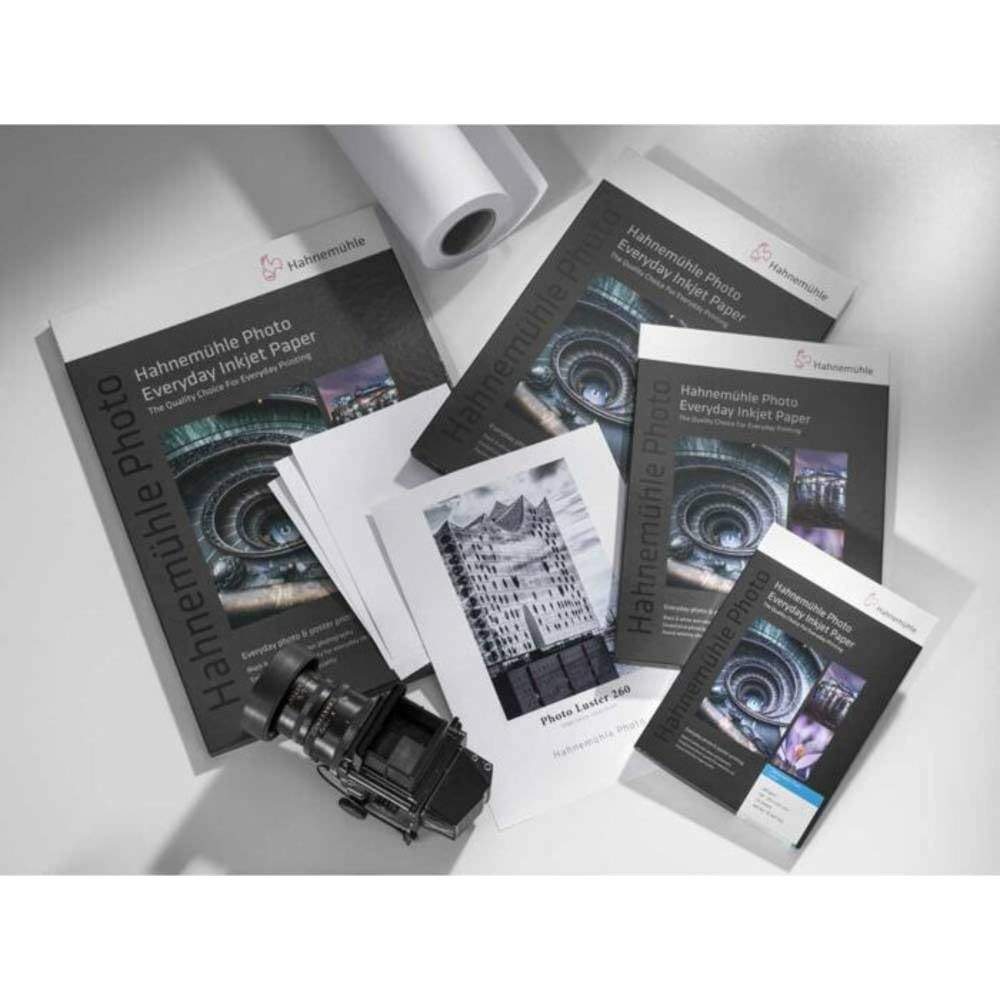 Hahnemühle Fotopapier-Packungen, eine Kameralinse und eine Papierrolle.