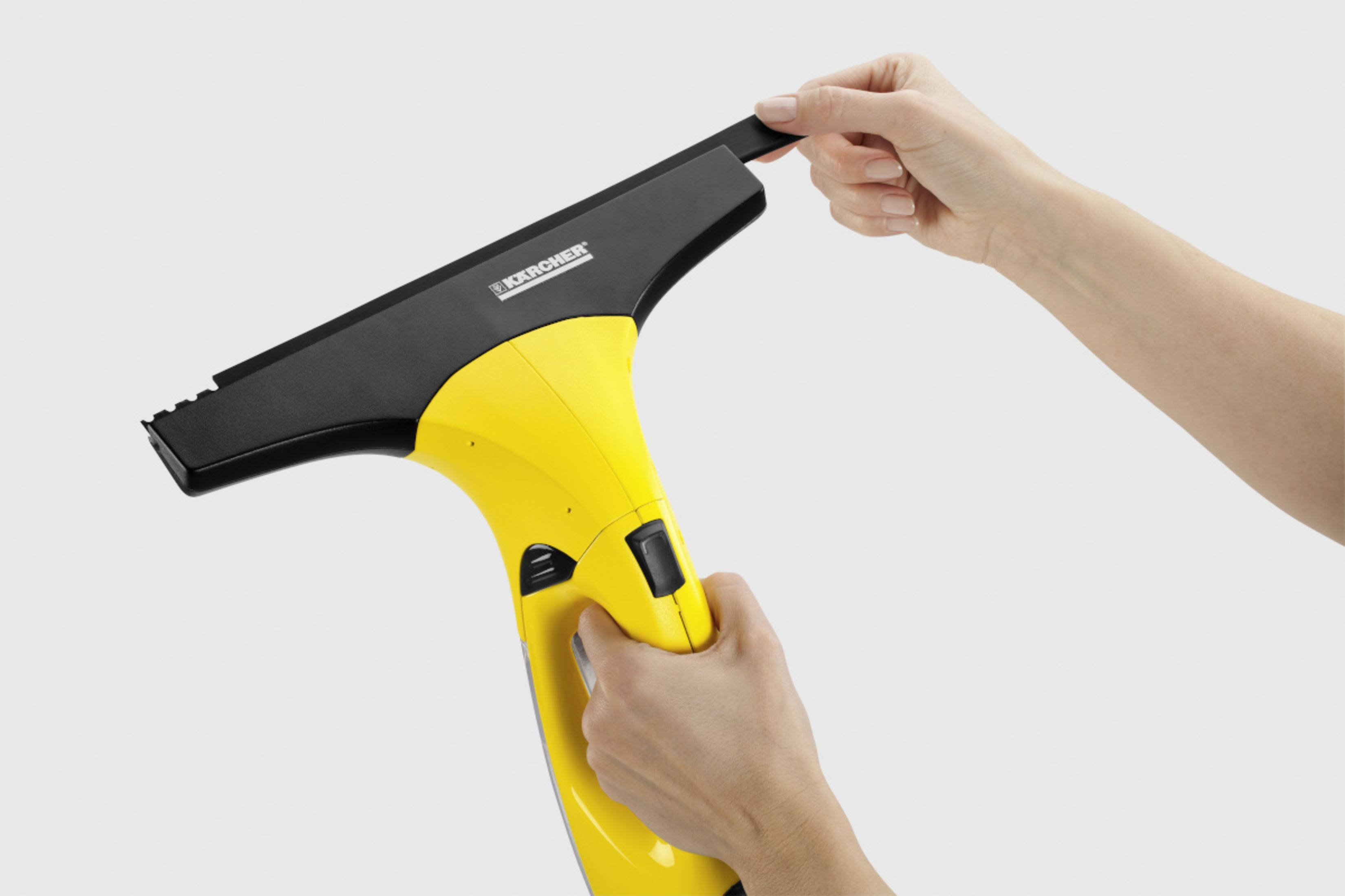 Yellow Karcher window cleaning device with black squeegee, held by hands.