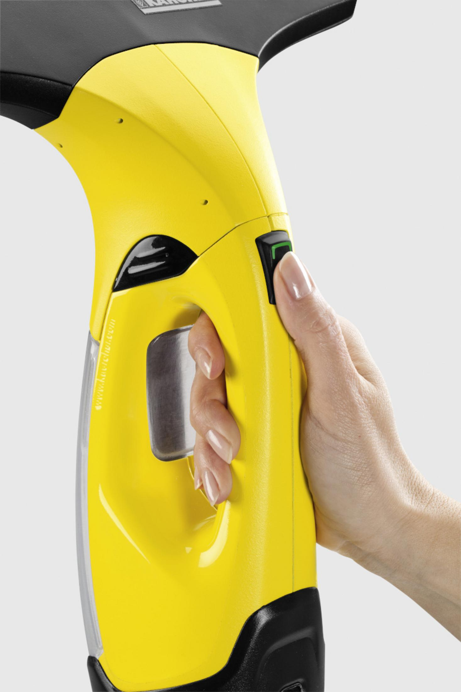 A hand grips a yellow window cleaner with a black handle. A green button is visible.
