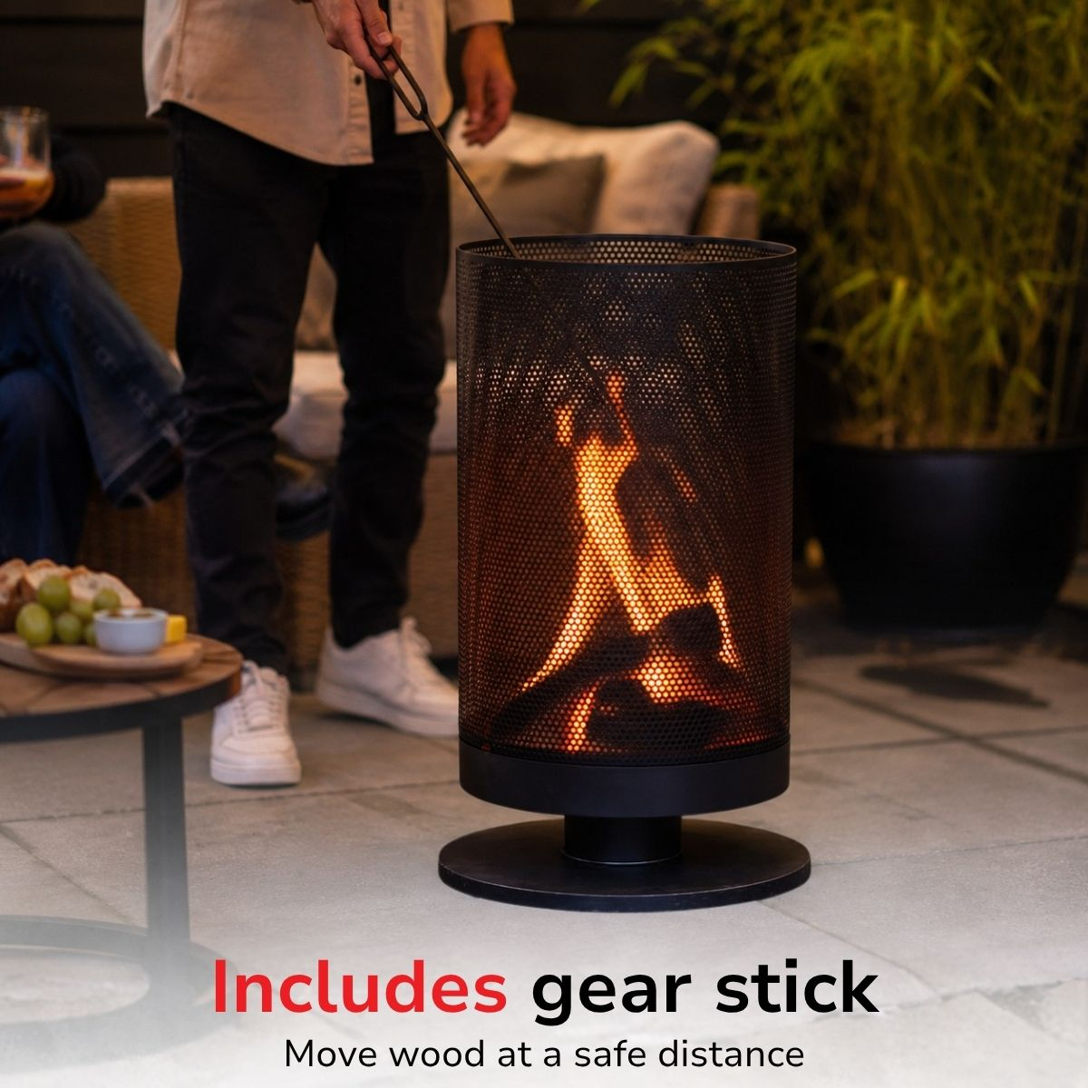 Person uses a gear stick to tend a fire in a black outdoor fireplace.