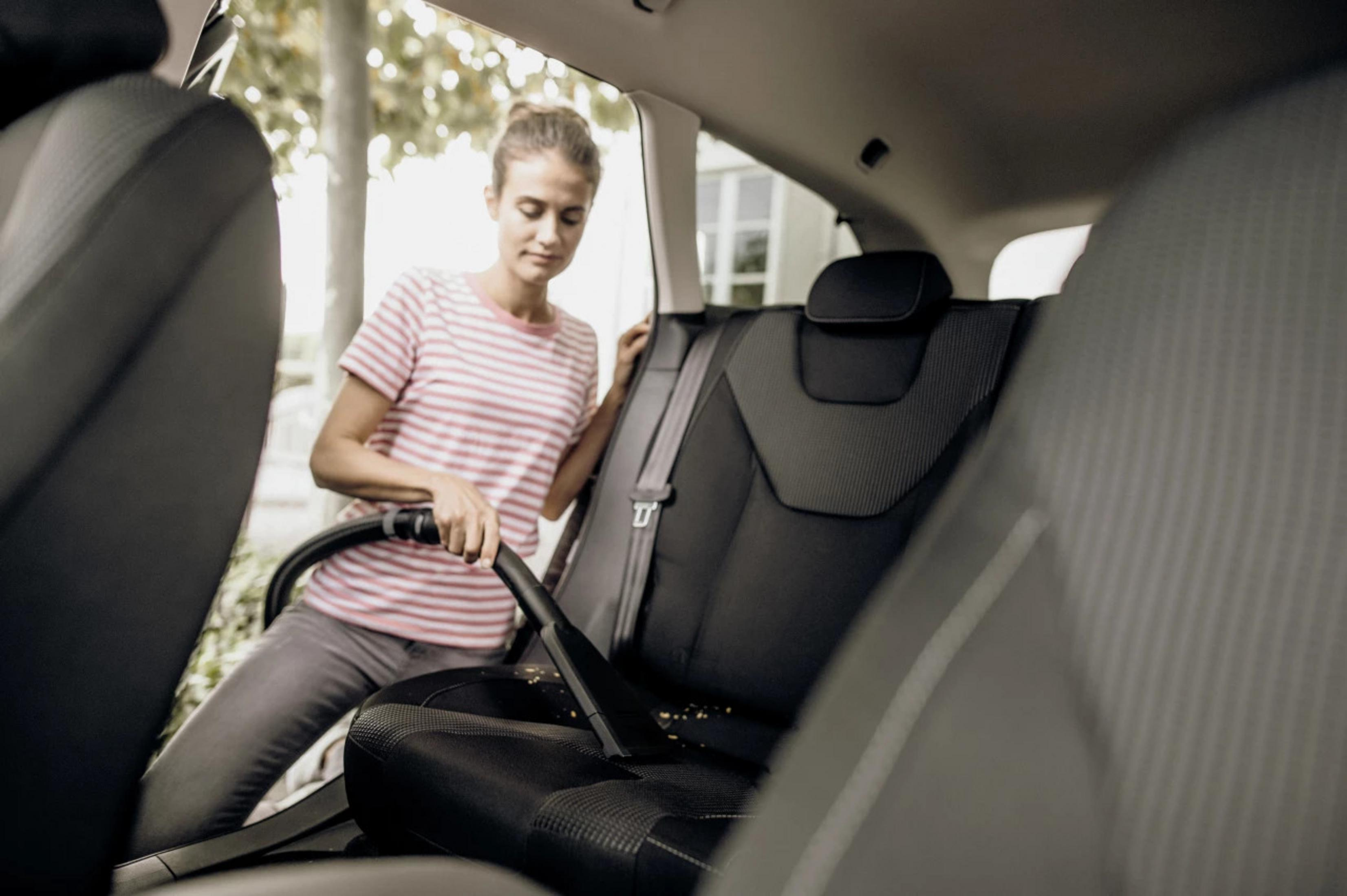 Eine Frau saugt einen Autositz mit einem Handstaubsauger.
