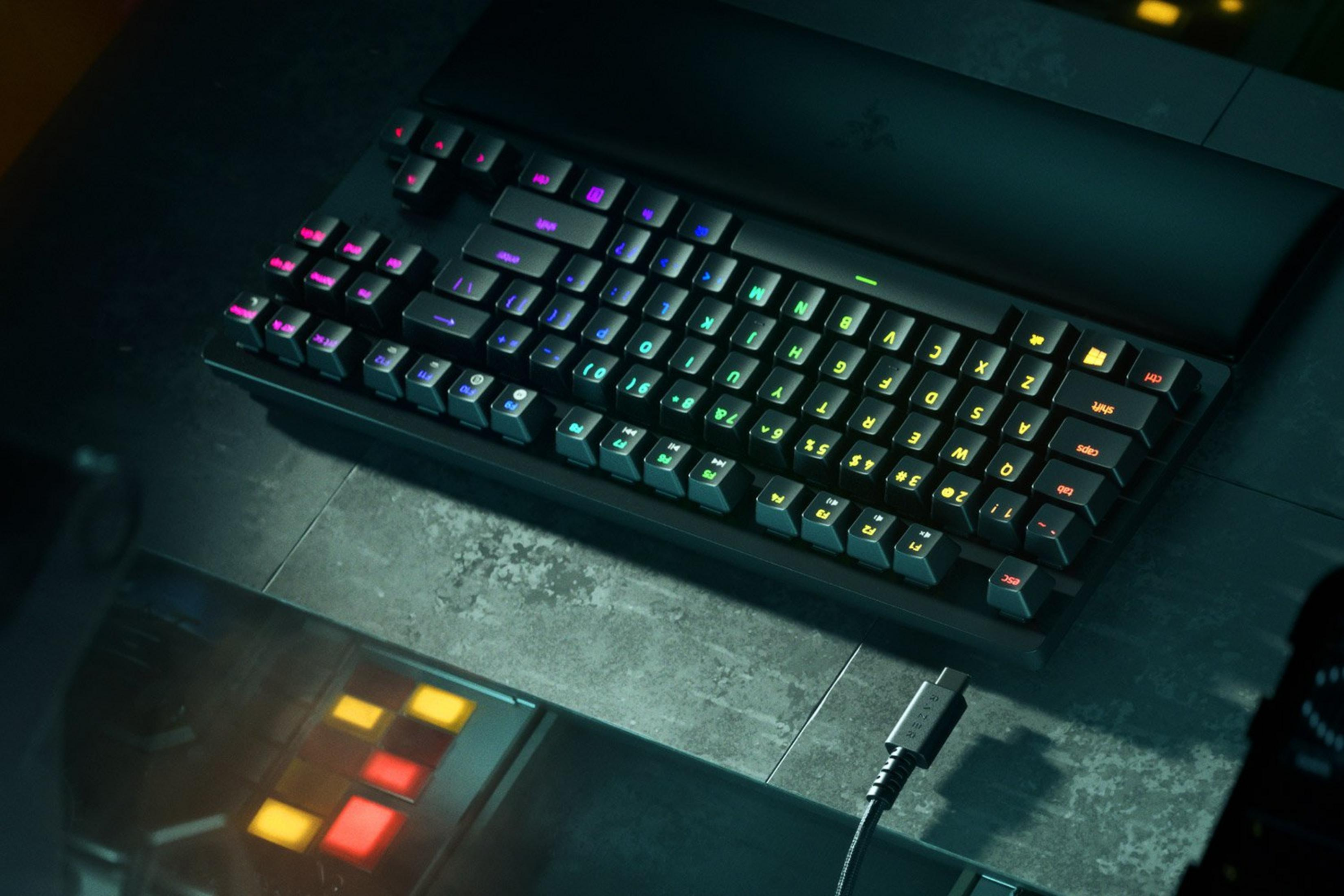 Una tastiera nera con illuminazione RGB colorata su una superficie scura.