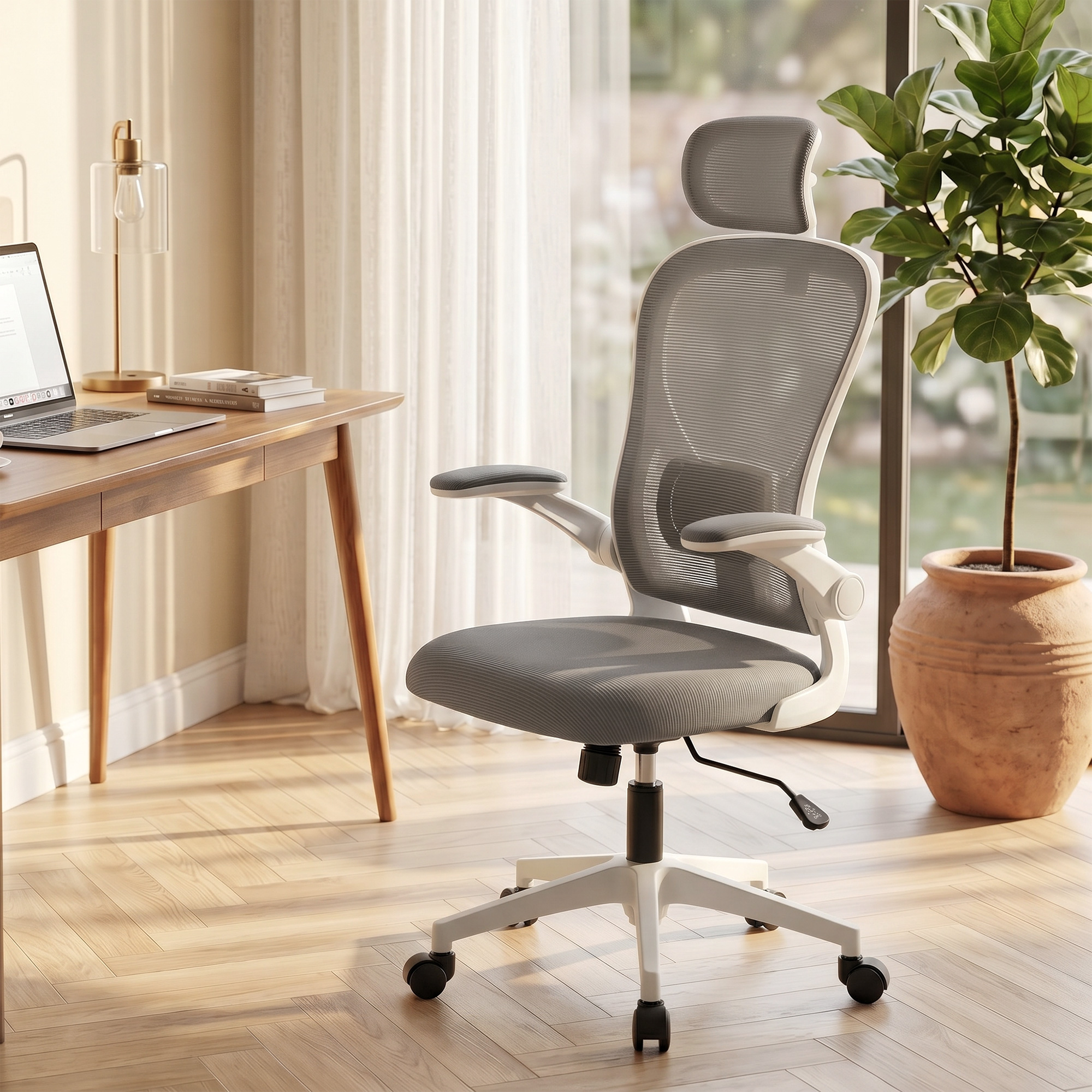 Una silla de oficina gris con reposacabezas junto a un escritorio de madera con portátil.