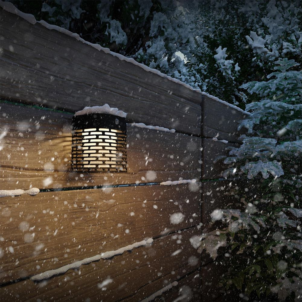 Lámpara de pared exterior en pared de madera nevando con árboles detrás.