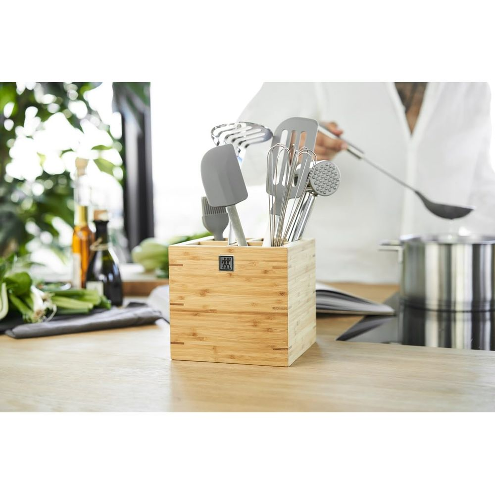 Blocco di legno con utensili da cucina, bottiglie d'olio e verdure a sinistra.