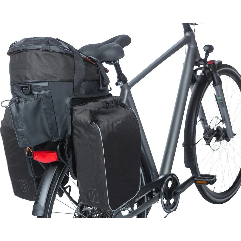 Ein schwarzes Fahrrad mit mehreren schwarzen Fahrradtaschen und einer Obertragetasche am Gepäckträger.