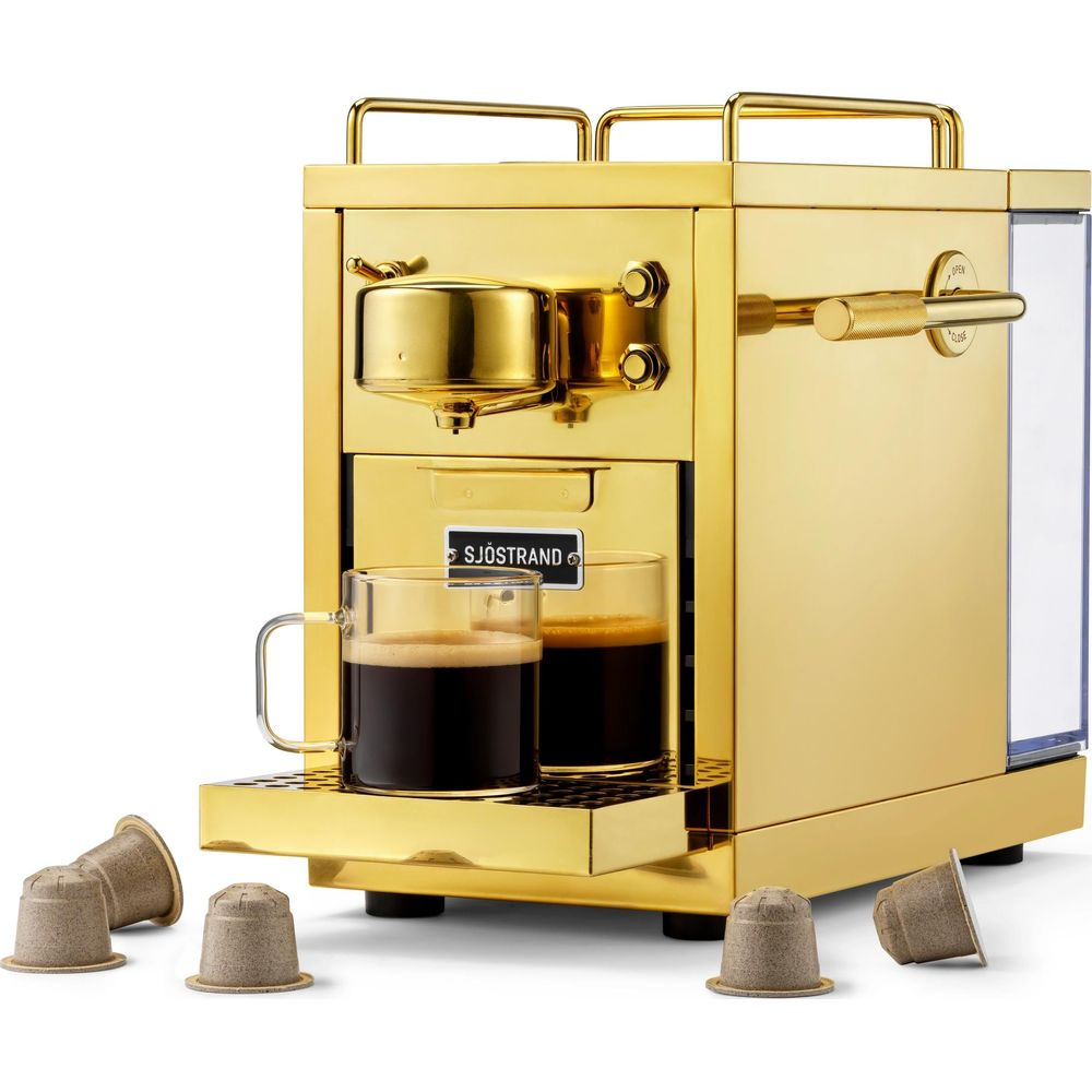 Macchina da caffè dorata con due tazze di espresso e capsule.