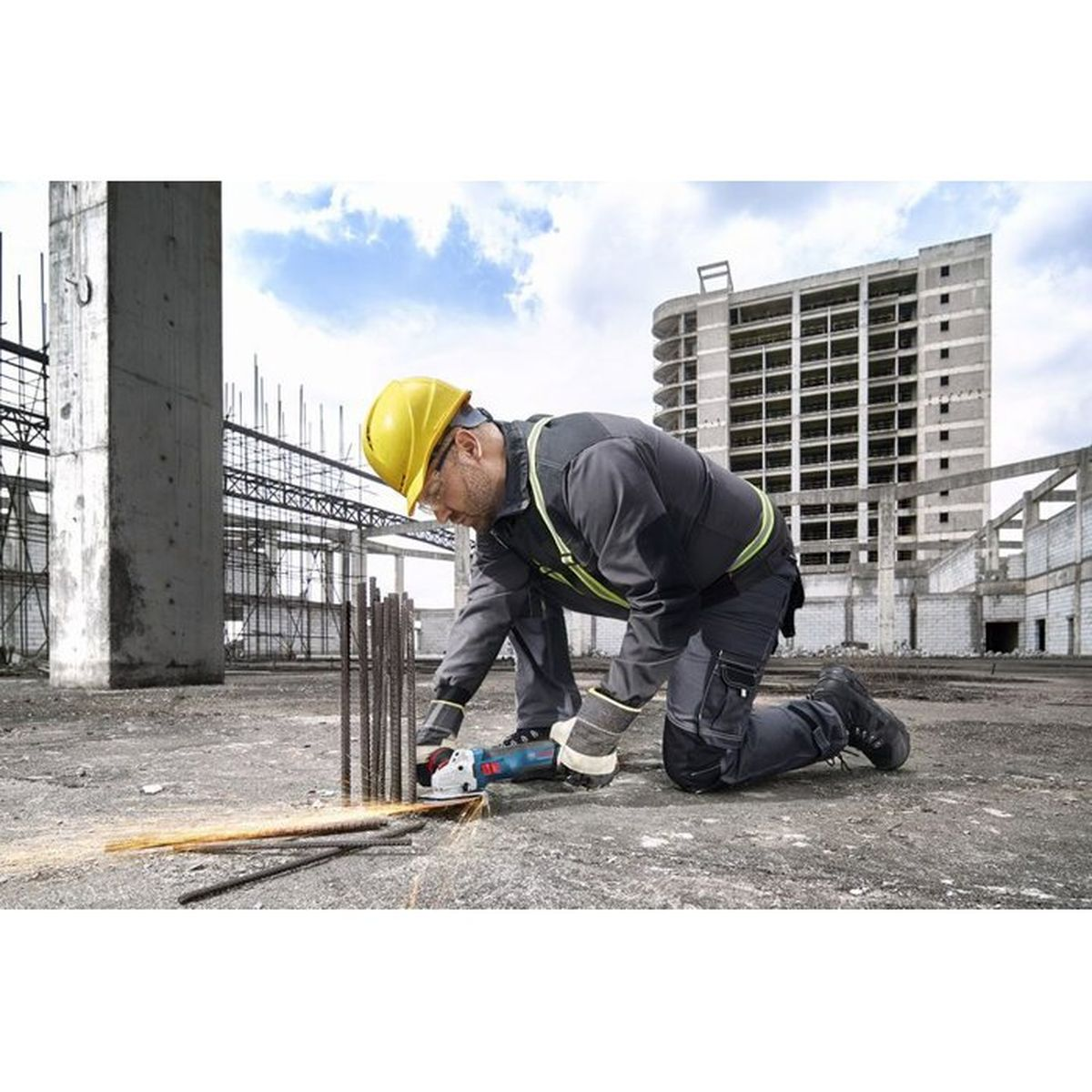 Ein Bauarbeiter mit gelbem Helm schneidet mit einem Winkelschleifer Metallstäbe auf einer Baustelle.
