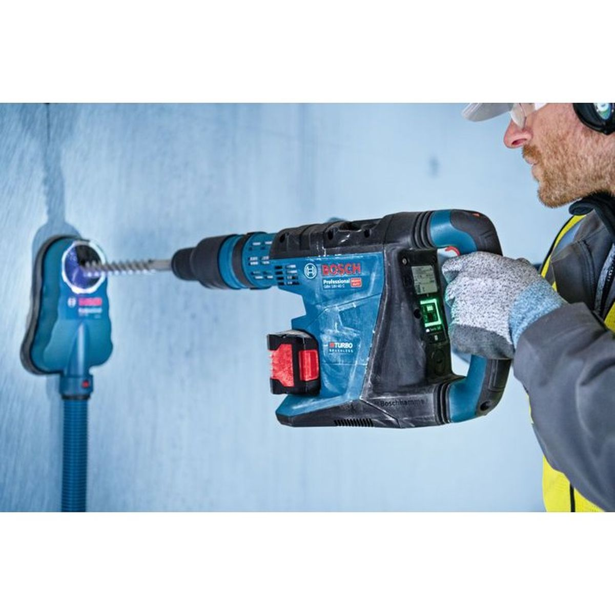 Mann bohrt mit blauer Bosch Bohrmaschine in Wand. Staubabsaugung ist montiert.
