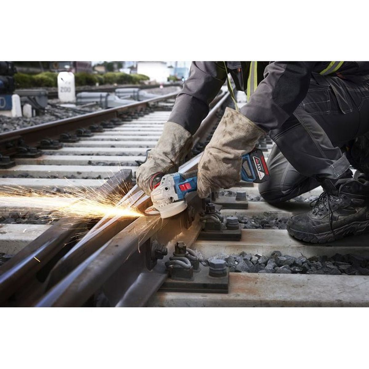 Ein Arbeiter schleift mit einem Winkelschleifer auf Bahngleisen, Funken sprühen.