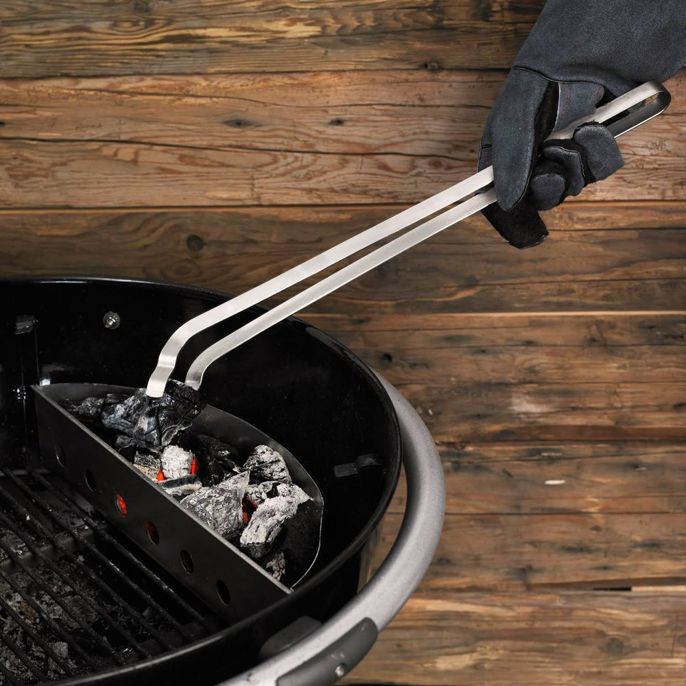 Glove hält Grillzange über Holzkohle in einem Grill.