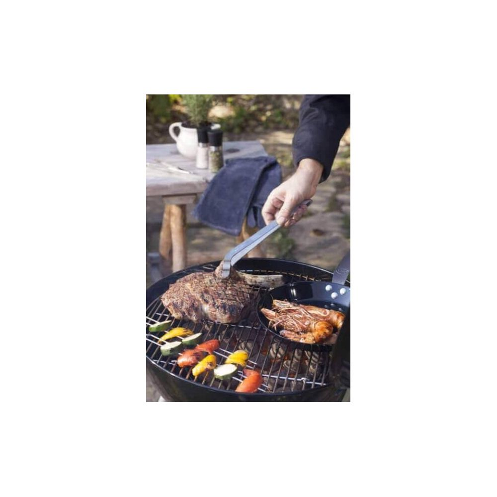 Steak und Garnelen auf Grill mit Gemüse. Hand dreht Steak mit Zange.