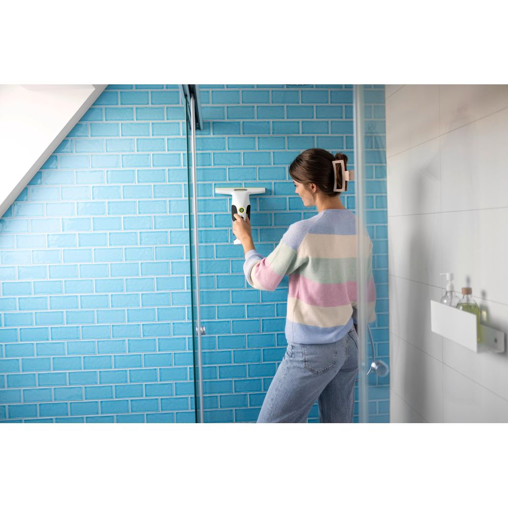 Eine Frau reinigt eine blaue Kachelwand in der Dusche mit einem Fensterreiniger.
