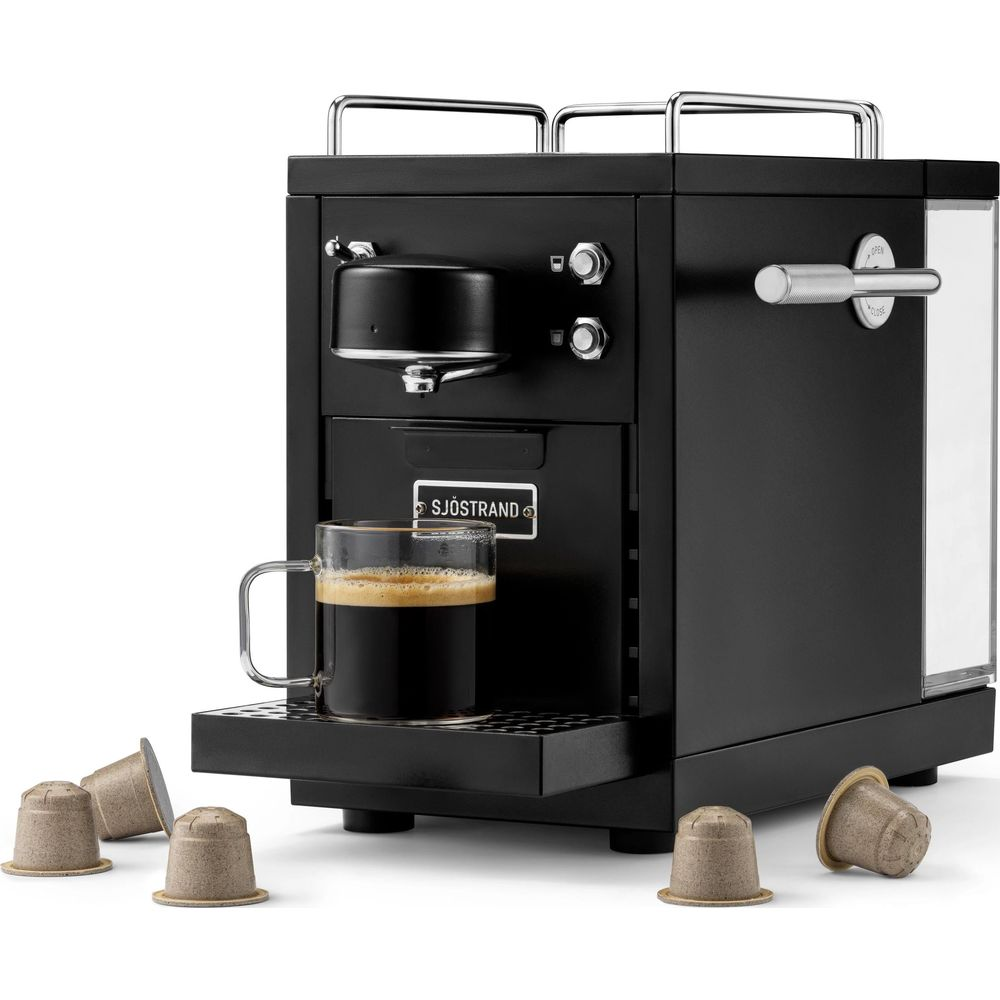 Macchina da caffè nera con tazza di vetro e capsule di caffè.