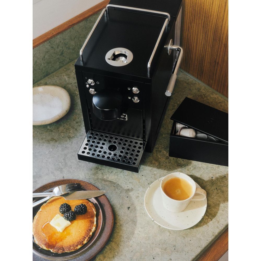 Una macchina da caffè nera con pancake e caffè su un piano di lavoro in marmo.