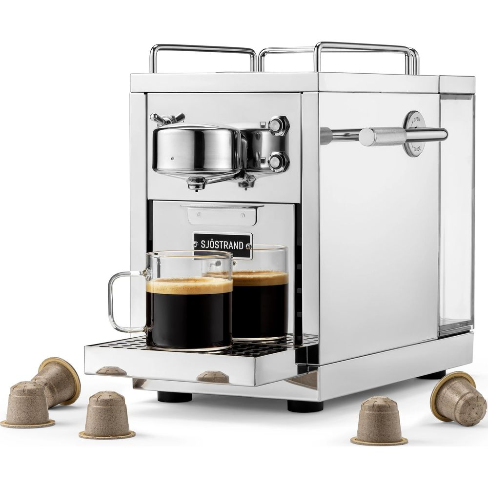 Macchina per espresso cromata con due tazze e capsule di caffè.