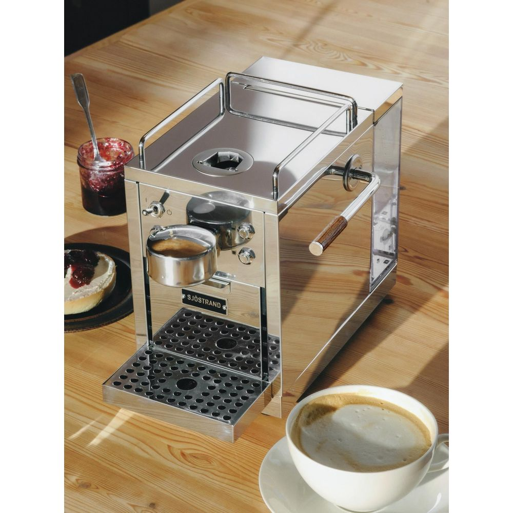 Macchina per espresso lucida su tavolo di legno con caffè e marmellata.