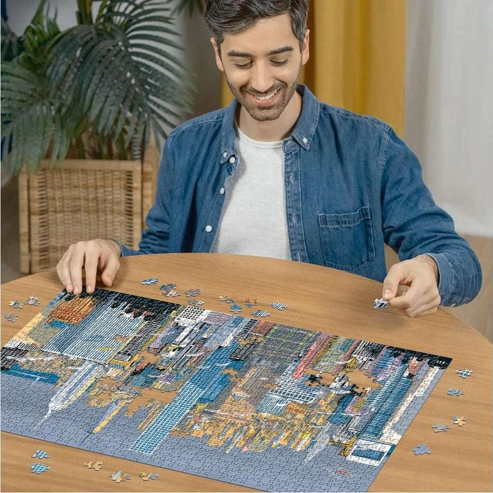 Mann baut Puzzles mit Stadtbild. Holztisch, Pflanze im Hintergrund.