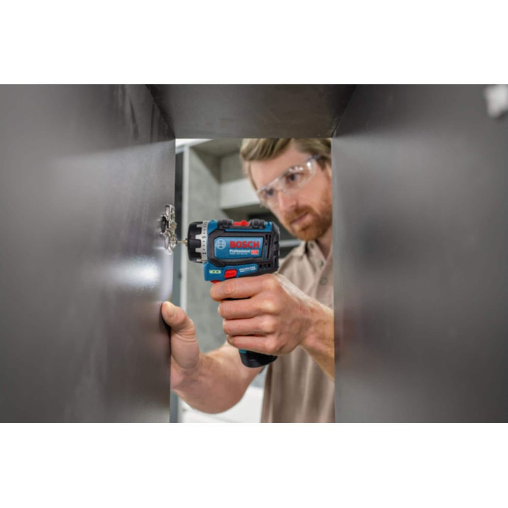 Hombre con gafas de seguridad taladra tornillo en superficie oscura con taladro Bosch azul.