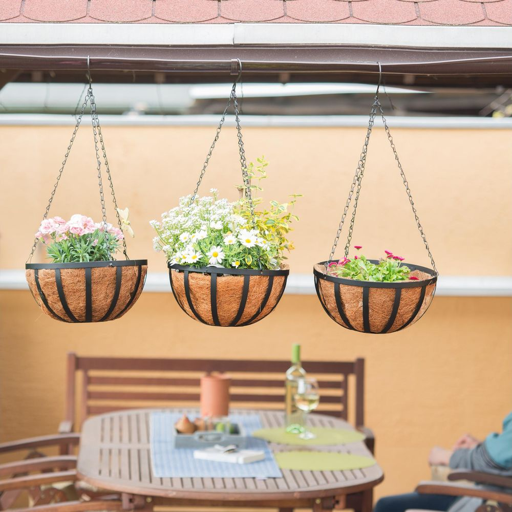 Drei hängende Körbe mit Blumen über einem Holztisch im Freien.