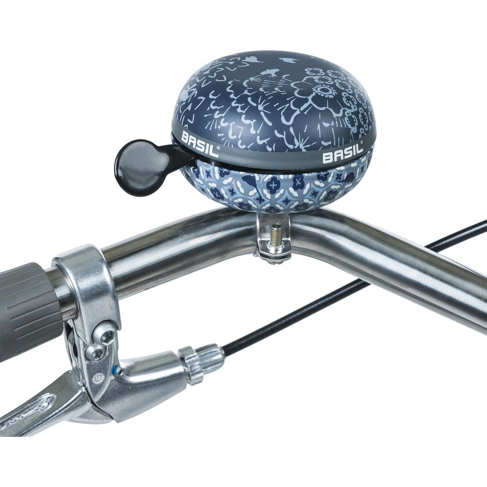 Ein blauer Fahrradklingel mit weißem Muster auf einem silbernen Lenker.